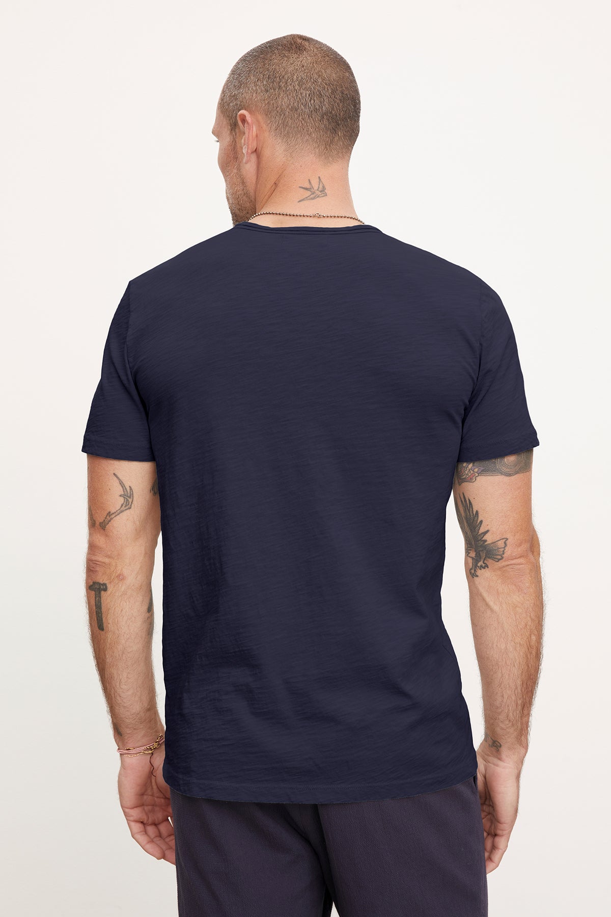   Rear view of a man wearing a Velvet by Graham & Spencer Chad Tee, displaying multiple arm tattoos and a neck tattoo. 