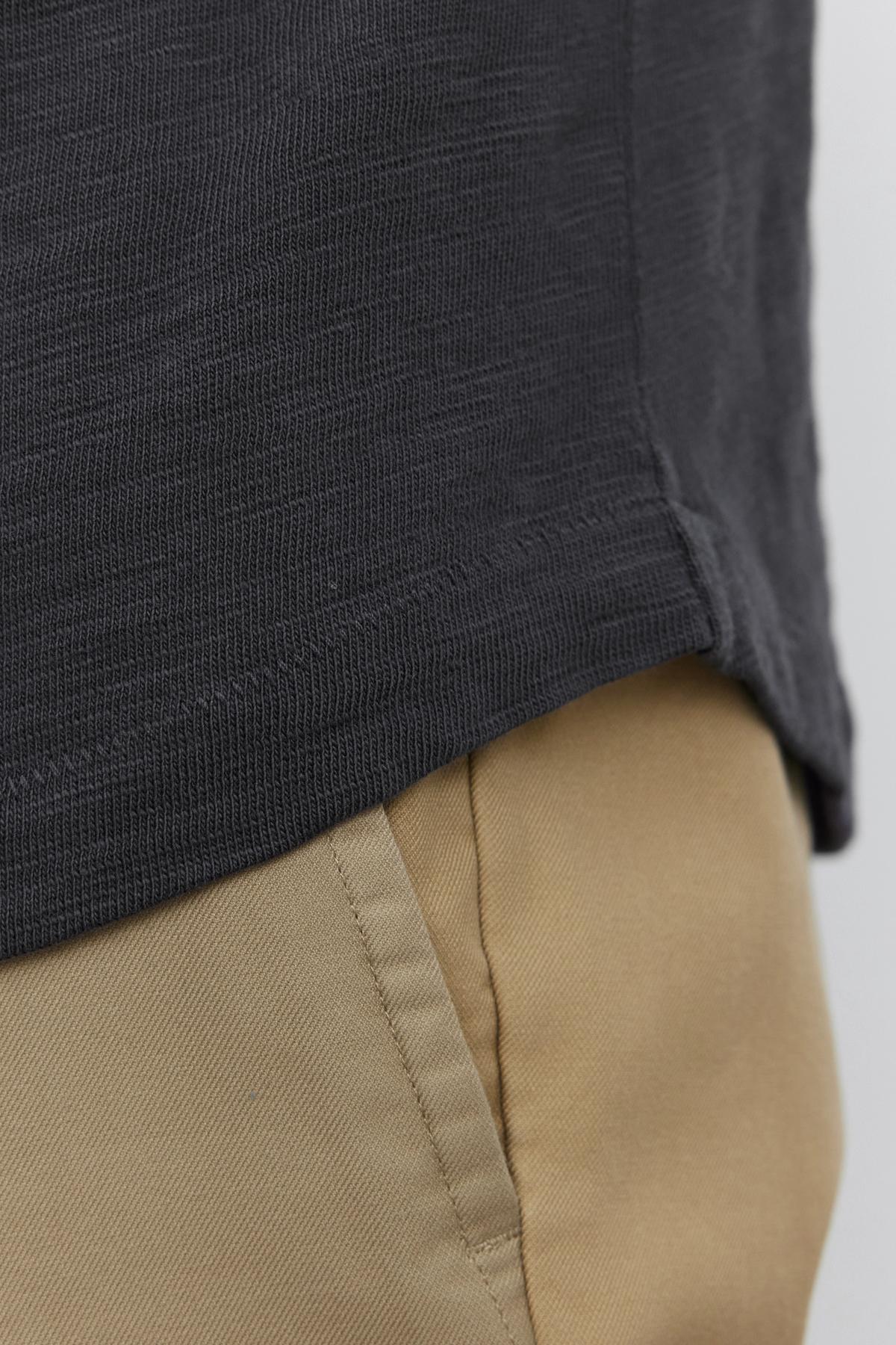   Close-up of a person wearing a black textured Velvet by Graham & Spencer SPADER TEE and beige pants with pockets. 