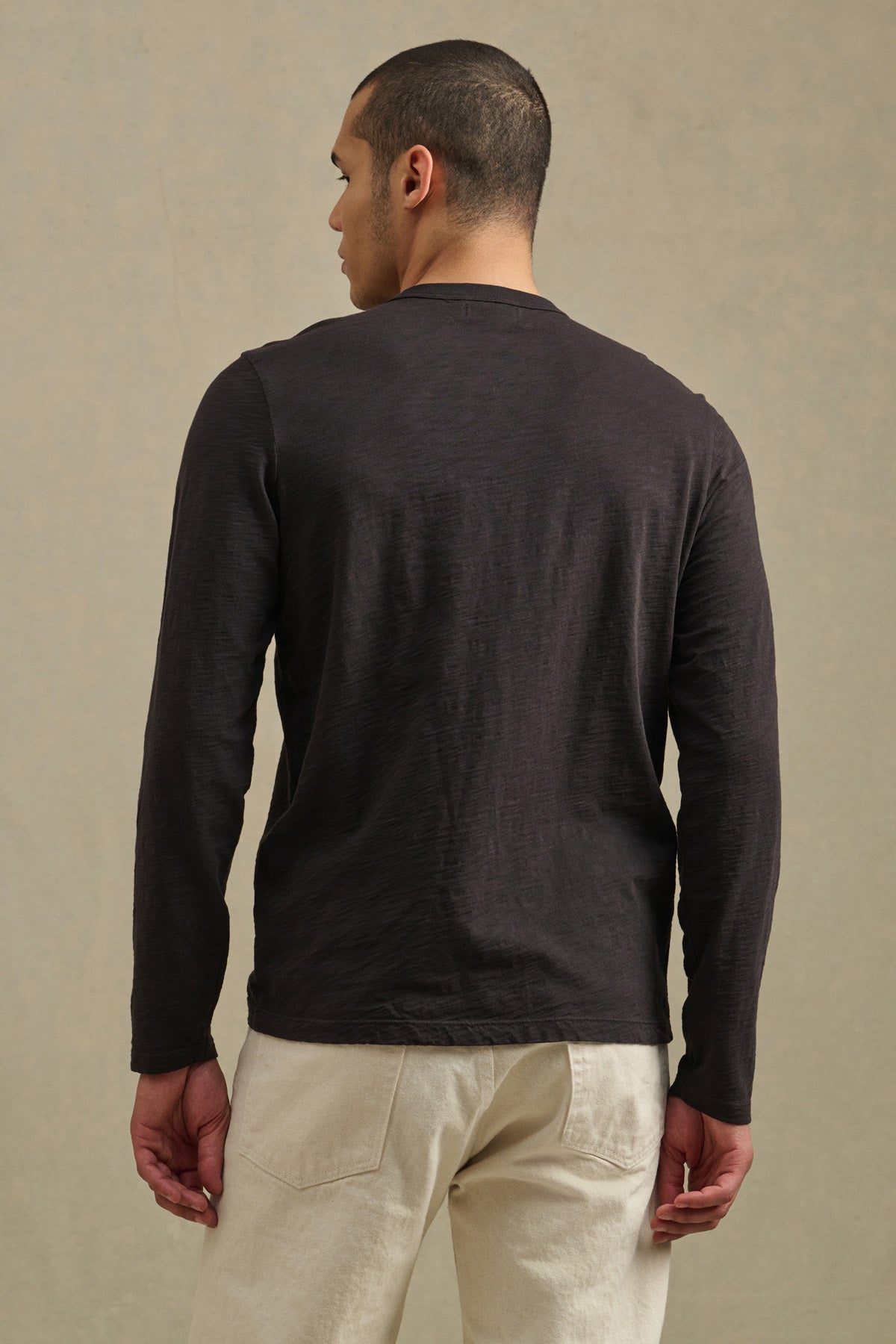 A person faces away from the camera, wearing the DALTON TEE by Velvet by Graham & Spencer with light-colored pants against a neutral background, highlighting timeless everyday style.