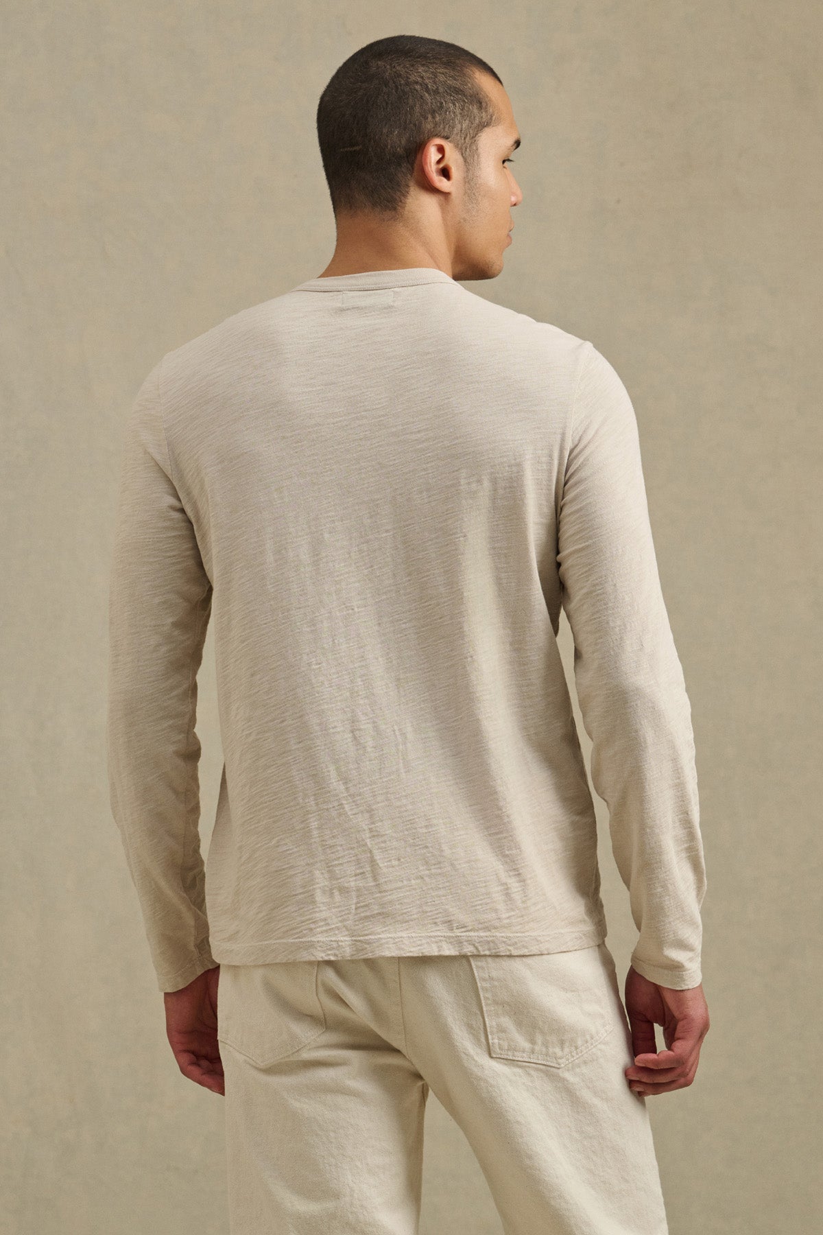 A man stands with his back turned, wearing the DALTON TEE by Velvet by Graham & Spencer—a long-sleeve cotton slub shirt with a crew neckline—paired with matching pants against a neutral background.