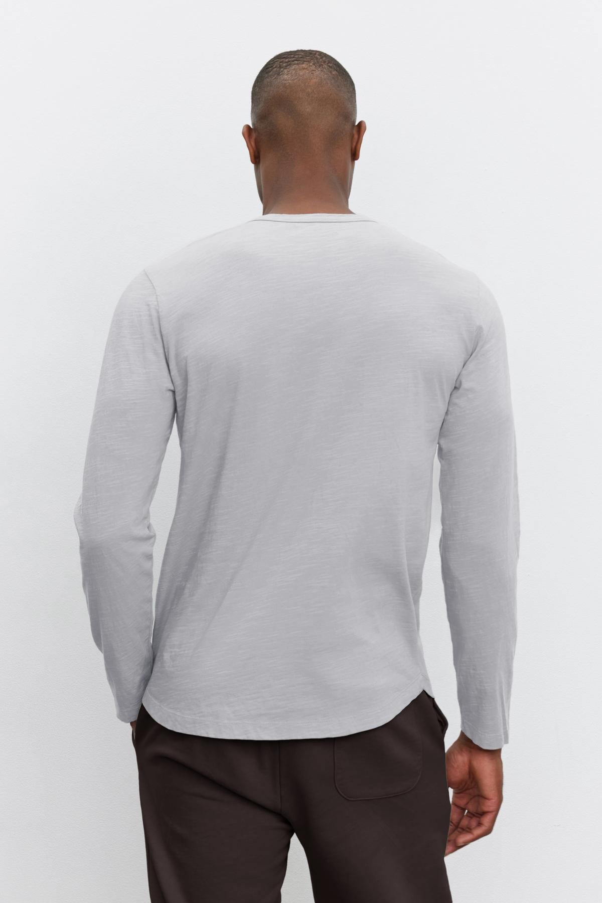   An individual wearing the KAI TEE in gray, designed by Velvet by Graham & Spencer, paired with dark pants is photographed from behind against a plain background, highlighting its timeless design. 