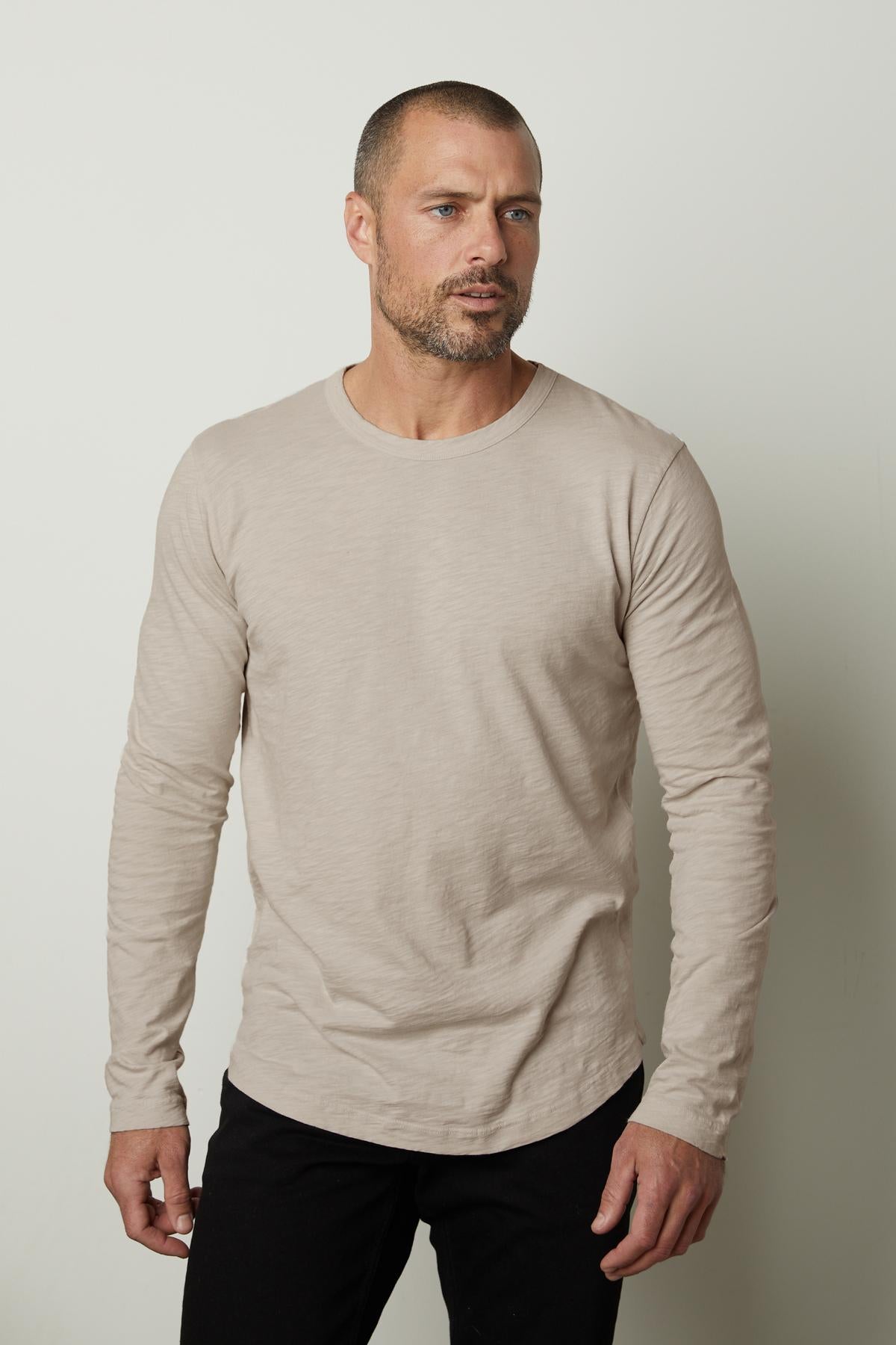   A man wearing a beige KAI CREW NECK TEE slub knit long-sleeve t-shirt from Velvet by Graham & Spencer, perfect for layering. 