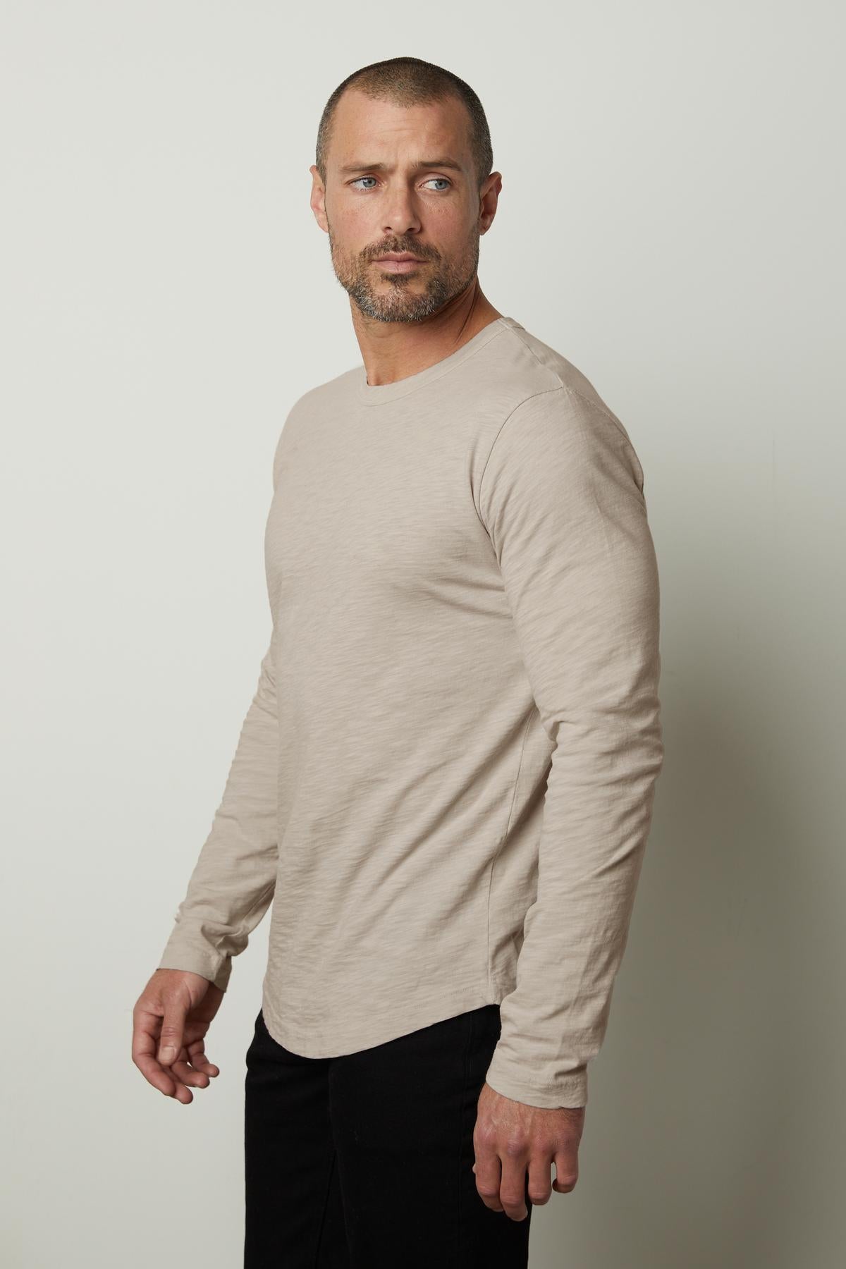 A man wearing a beige long sleeve KAI CREW NECK TEE by Velvet by Graham & Spencer, perfect for layering.-35776214597825