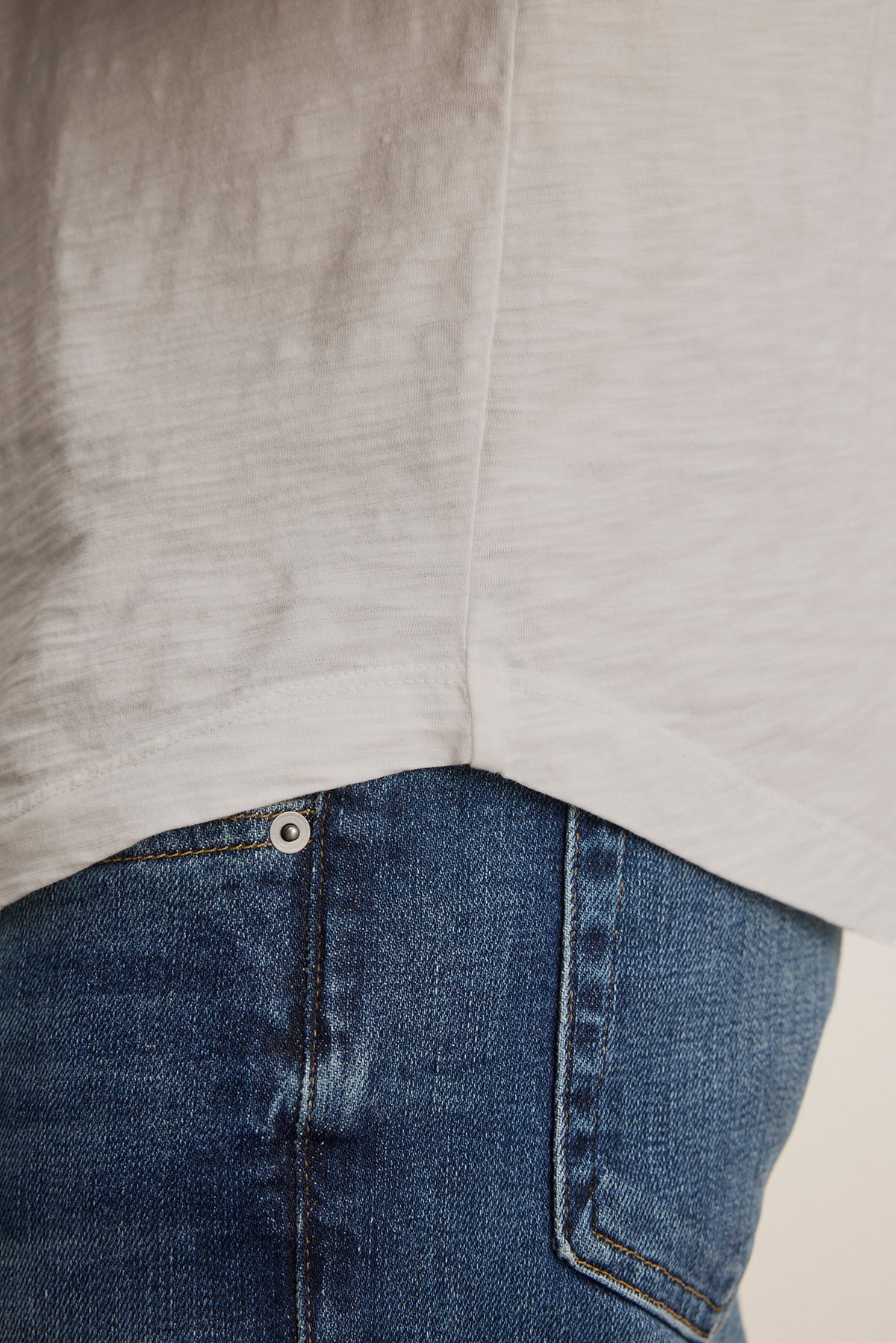   Close-up of someone wearing the lightweight KAI TEE by Velvet by Graham & Spencer and blue jeans, highlighting the crew neck and side seam of the shirt along with the timeless pocket detail on the jeans. 