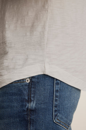 Close-up of someone wearing the lightweight KAI TEE by Velvet by Graham & Spencer and blue jeans, highlighting the crew neck and side seam of the shirt along with the timeless pocket detail on the jeans.