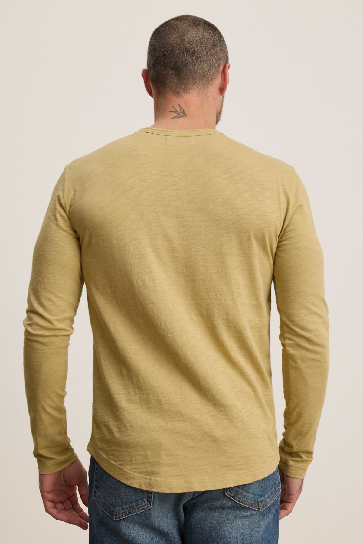 A man is shown from the back wearing the light yellow KAI TEE by Velvet by Graham & Spencer with blue jeans, revealing a small bird tattoo on his neck.-39957108719809