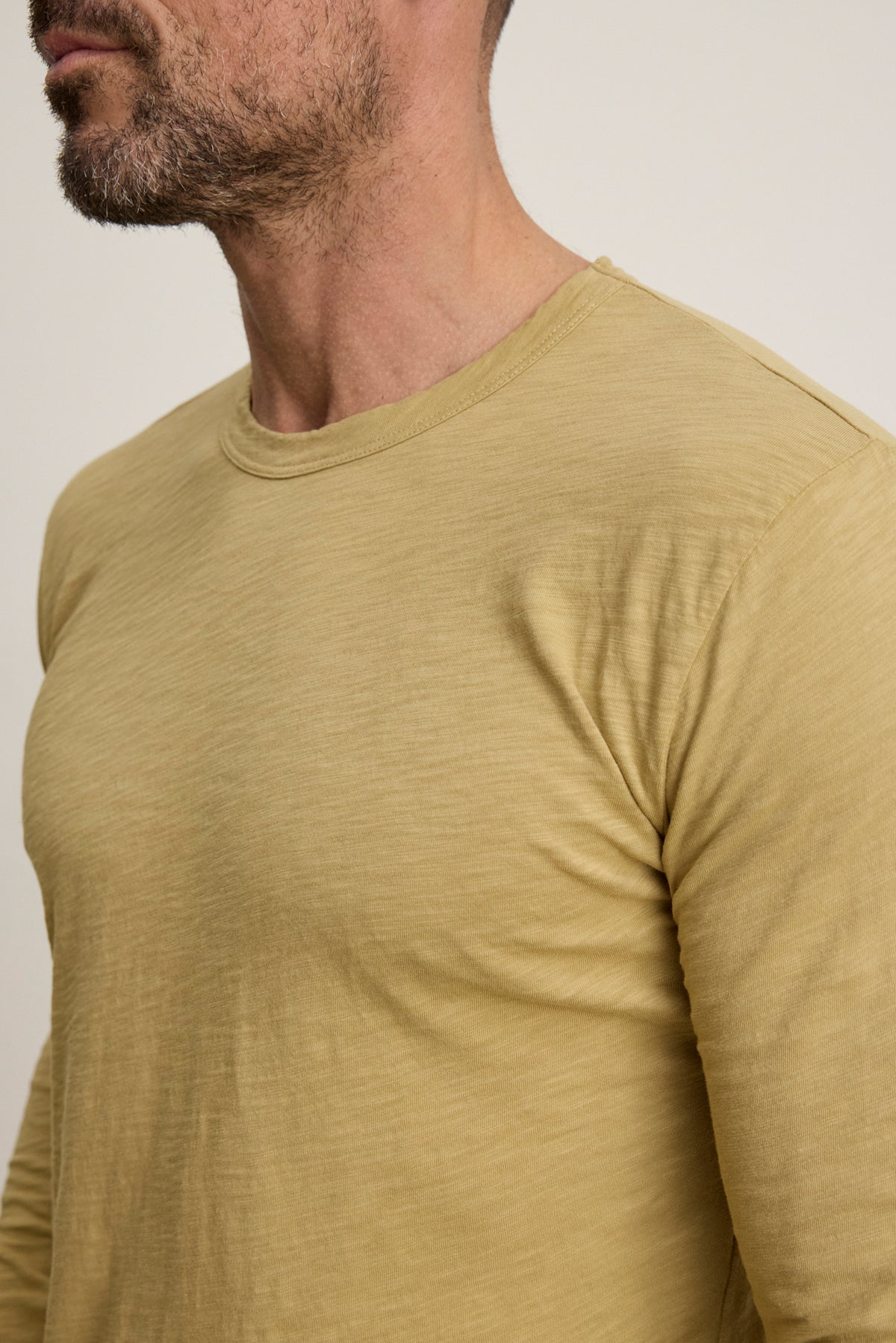 A bearded man, shown from the chest up and facing slightly left, wears a light yellow KAI TEE long sleeve crewneck by Velvet by Graham & Spencer.-39957108752577