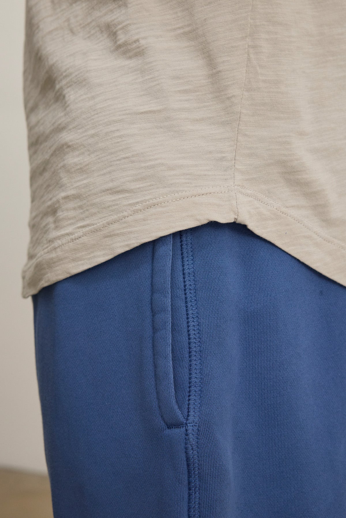 Close-up of a person in blue pants and the KAI TEE by Velvet by Graham & Spencer, featuring soft beige Peruvian cotton, crew neckline, and detailed seams.