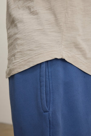 Close-up of a person in blue pants and the KAI TEE by Velvet by Graham & Spencer, featuring soft beige Peruvian cotton, crew neckline, and detailed seams.