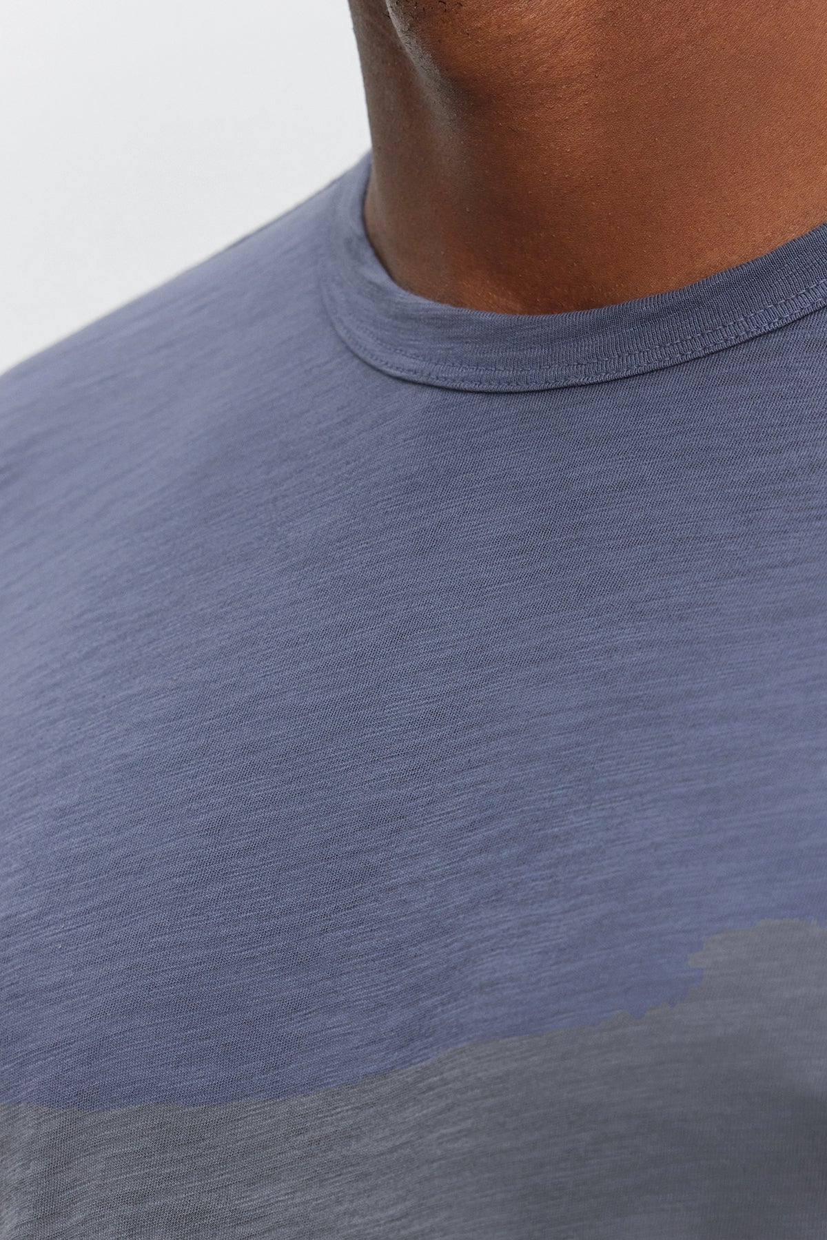 Close-up of a person wearing the KAI TEE, a blue crew neck t-shirt made from Peruvian cotton by Velvet by Graham & Spencer. Only the lower half of their face and the upper torso are visible, showcasing the timeless design and classic crew neckline.-37893903286465