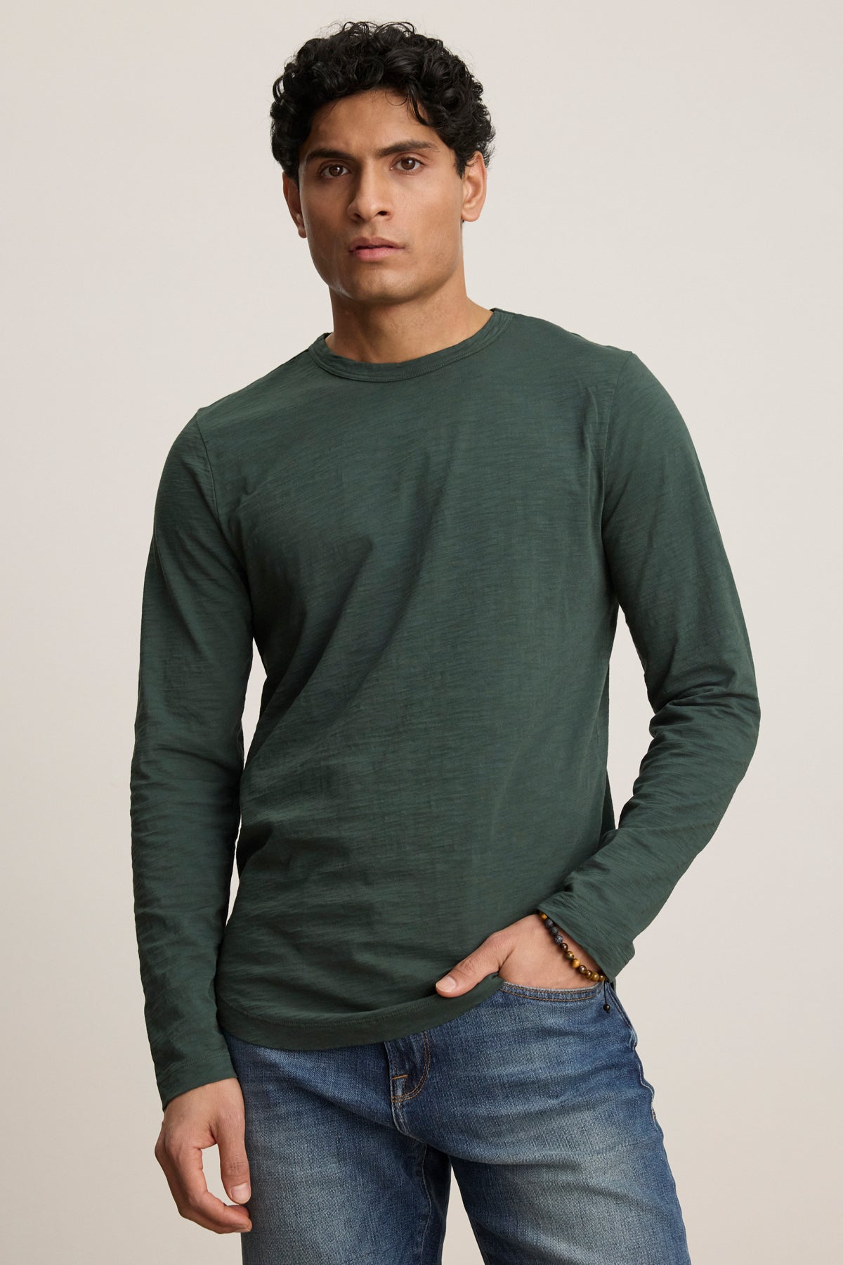 A person wearing the Velvet by Graham & Spencer KAI TEE, a classic crew neckline long sleeve shirt in dark green, and blue jeans stands against a plain light background.-39905775124673