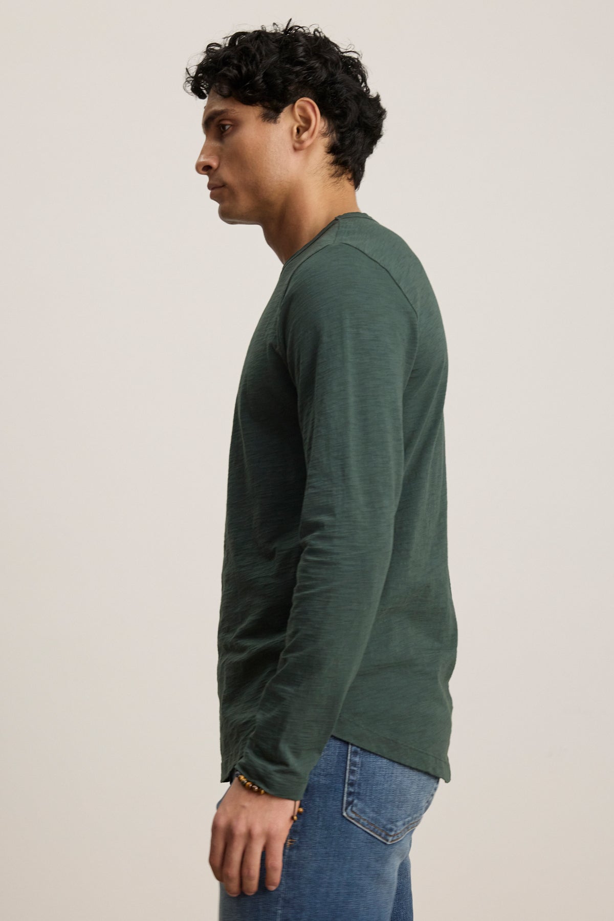A man in profile wears the Velvet by Graham & Spencer KAI TEE, a long sleeve crew neck shirt, with blue jeans against a plain light background.-39905775026369
