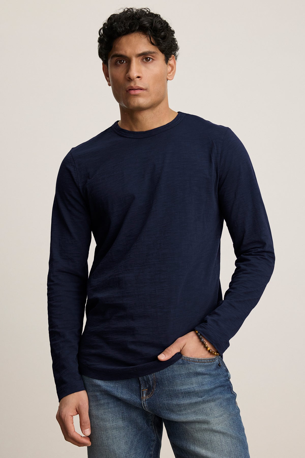   A model wearing Velvet by Graham & Spencer's KAI TEE, featuring a crew neckline and long sleeves, paired with jeans against a plain background. 