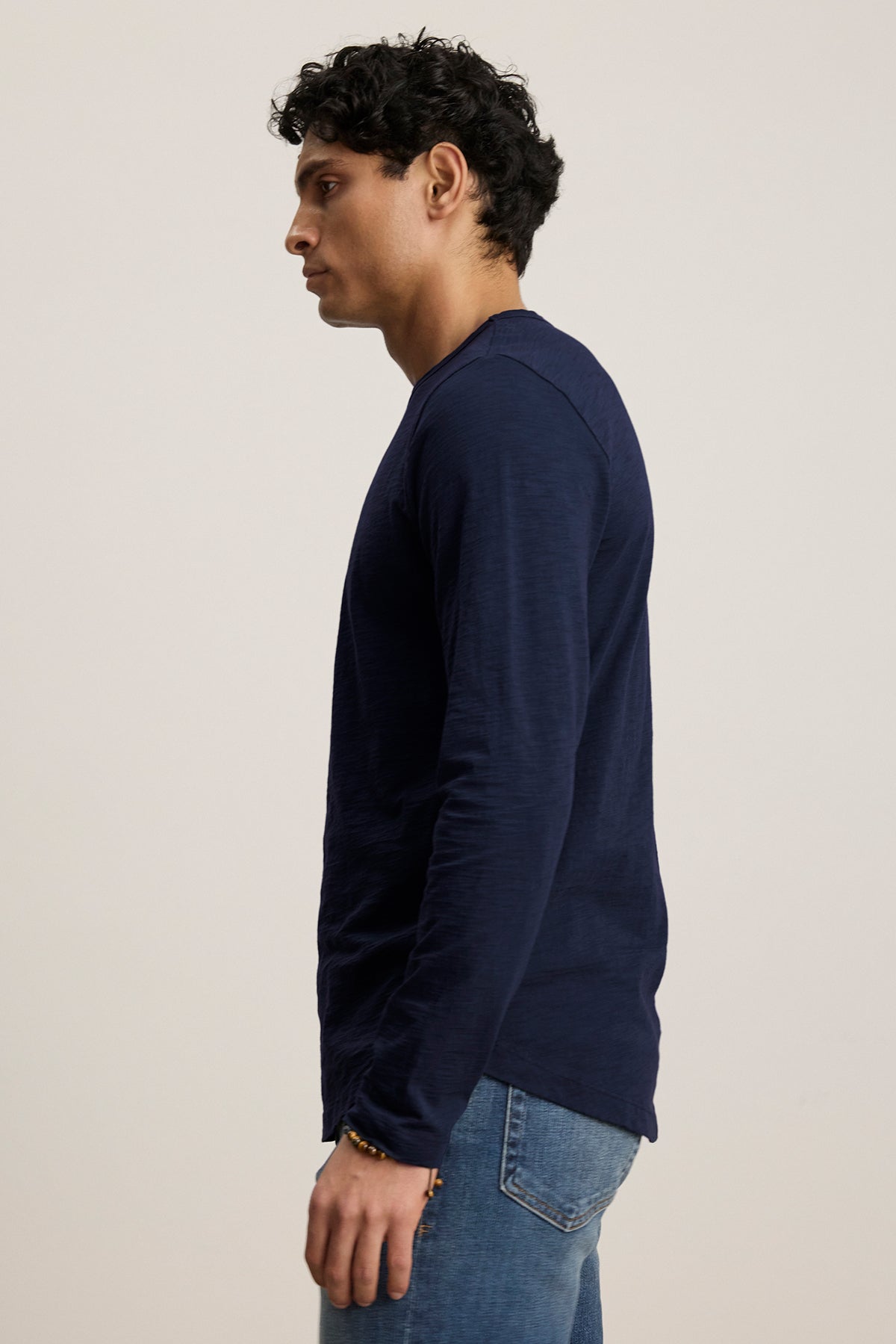   A person in a Velvet by Graham & Spencer KAI TEE, featuring classic navy long sleeves and paired with jeans, poses sideways against a plain background to highlight its timeless design. 