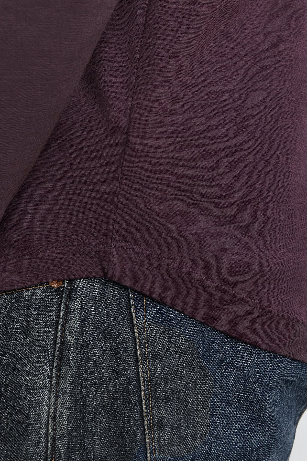   Close-up photo showing the lower part of a person wearing a dark purple KAI TEE by Velvet by Graham & Spencer and dark blue denim jeans. 