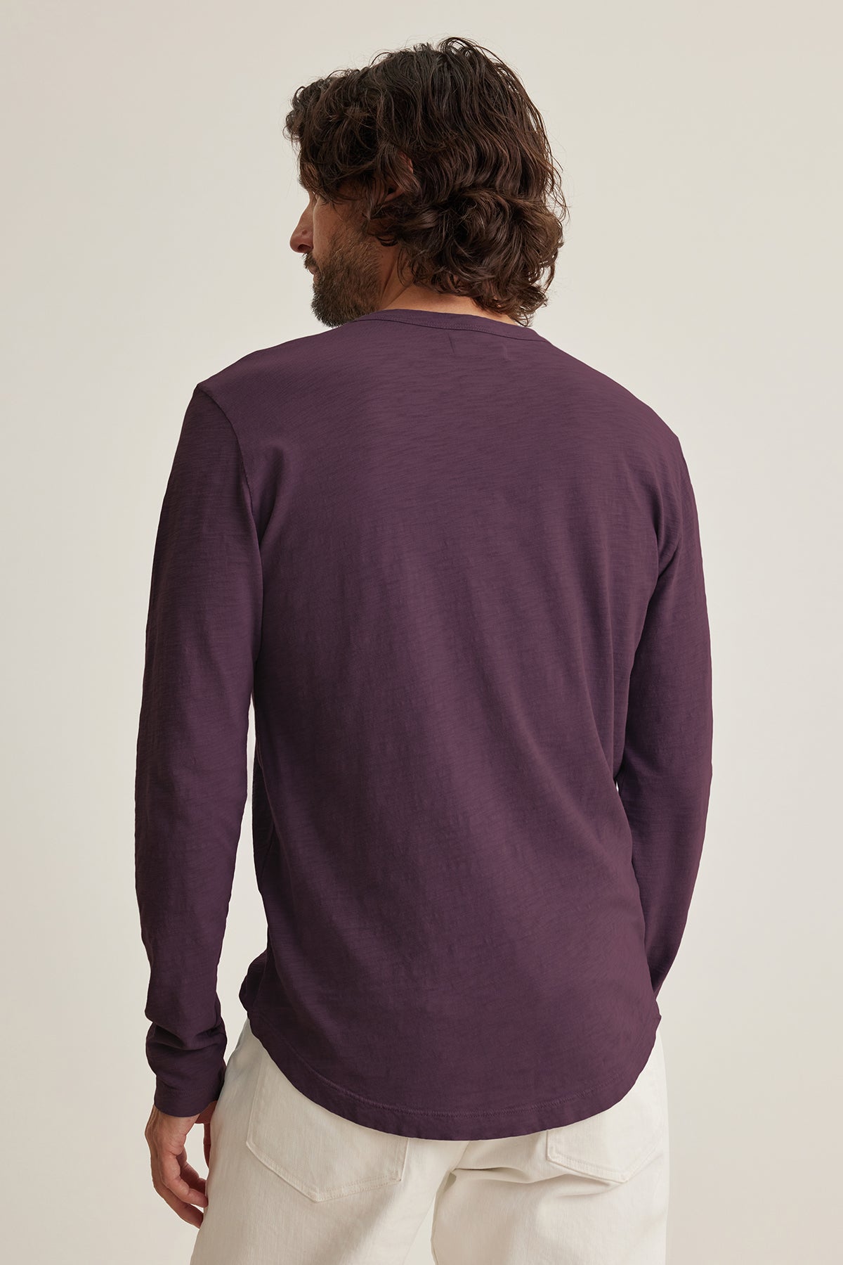 A dark-haired man wears a maroon KAI TEE by Velvet featuring a crew neck, paired with light pants, and is facing away.-38807449206977