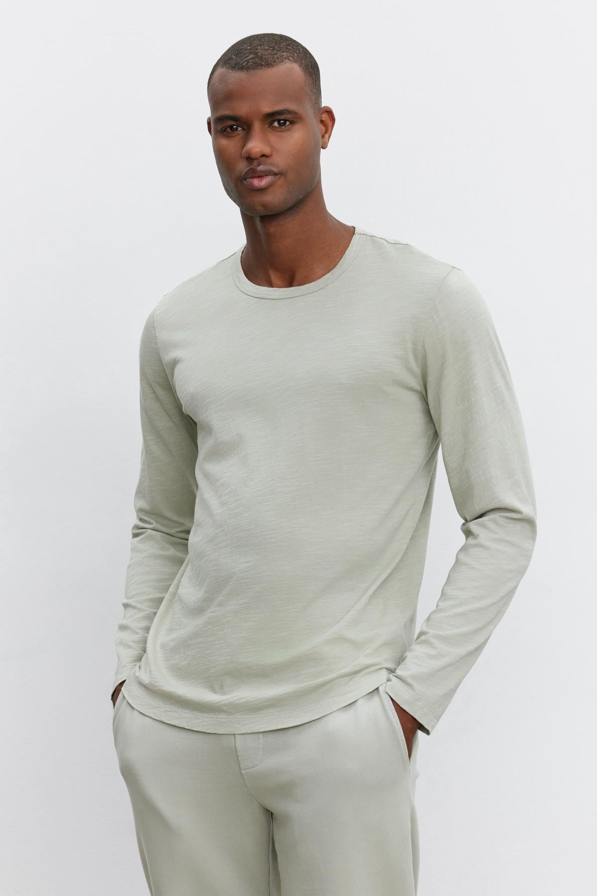   Man wearing a light green, long-sleeve KAI TEE by Velvet by Graham & Spencer with a classic crew neckline and light green pants, standing against a plain white background. The outfit is crafted from textured cotton slub for added dimension. 