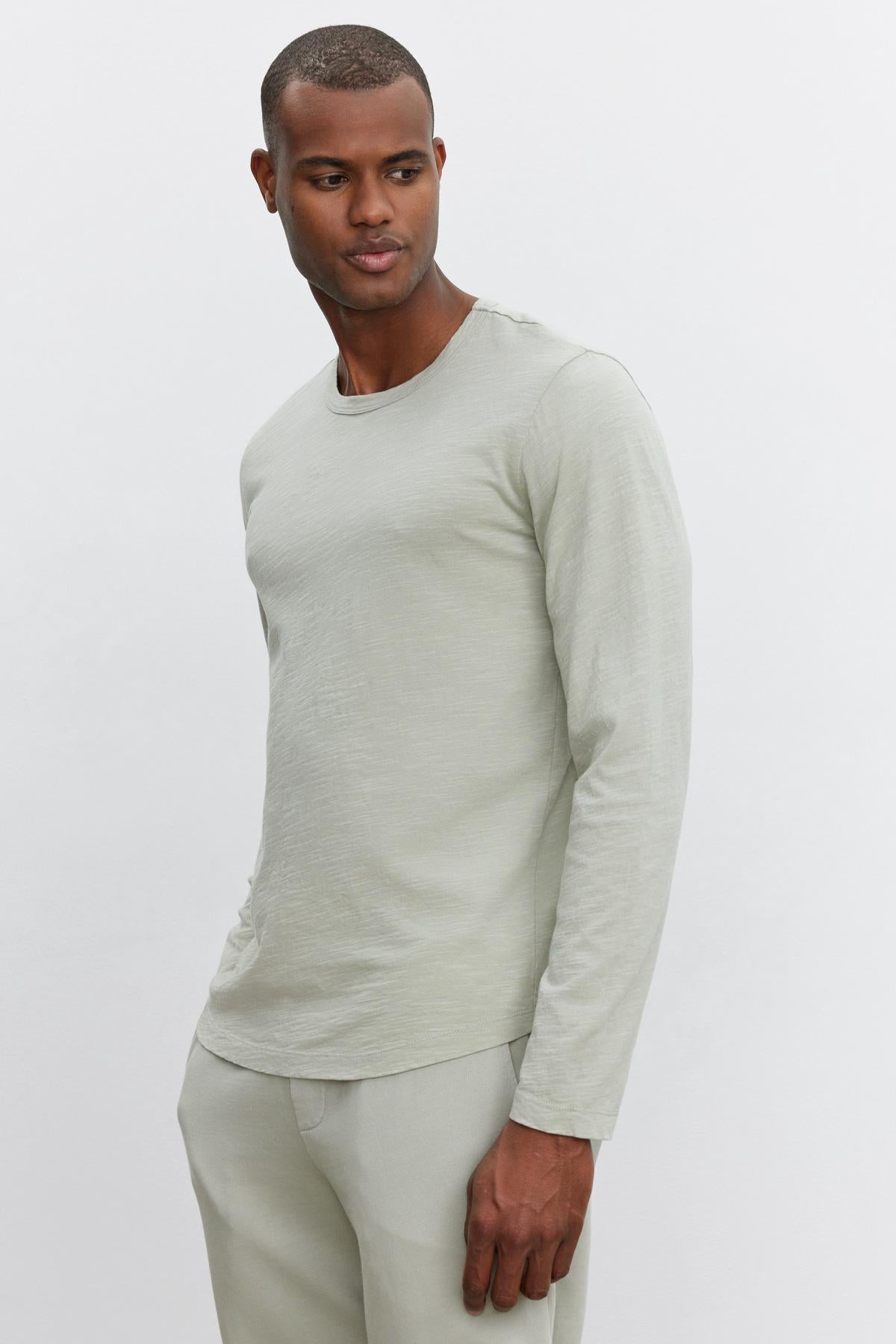   A person wearing a light gray long-sleeve KAI TEE shirt from Velvet by Graham & Spencer with a classic crew neckline and matching pants stands against a plain white background. 