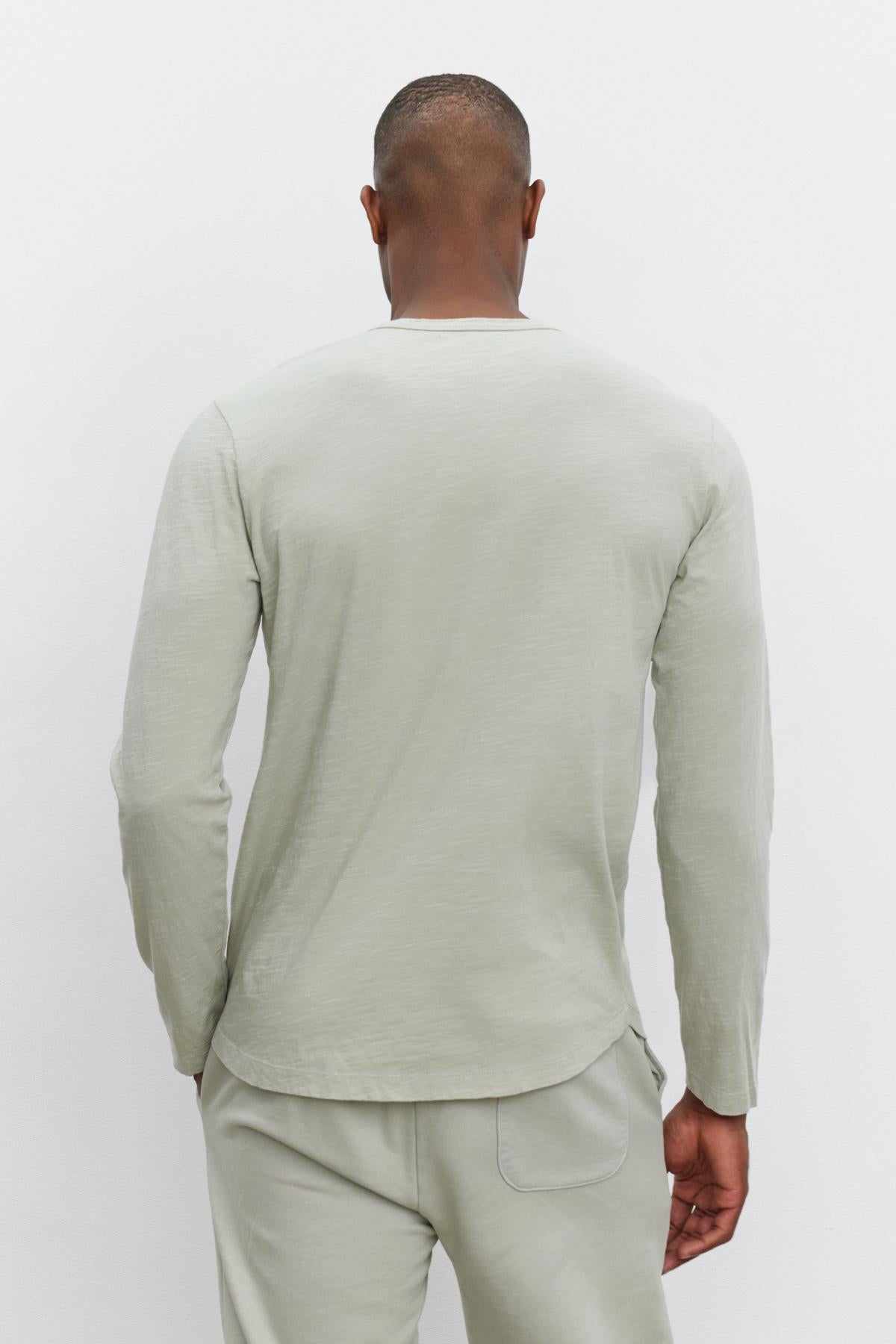   A person is seen from behind wearing a long-sleeve, light gray KAI TEE by Velvet by Graham & Spencer with a classic crew neckline and matching pants against a plain white background. 