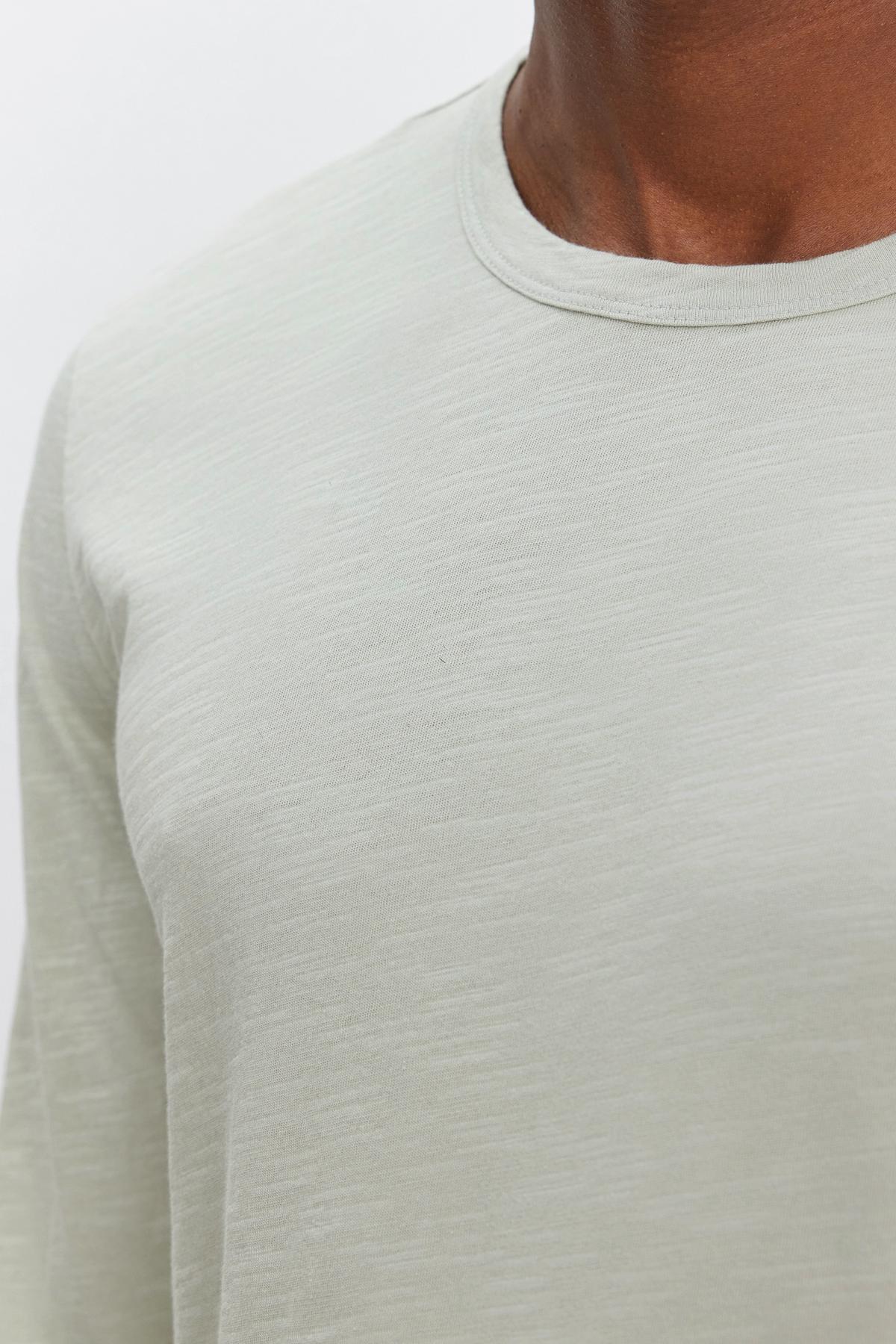   Close-up of a person wearing a light grey, textured cotton slub long-sleeve shirt with a classic crew neckline (KAI TEE by Velvet by Graham & Spencer) against a plain background. 