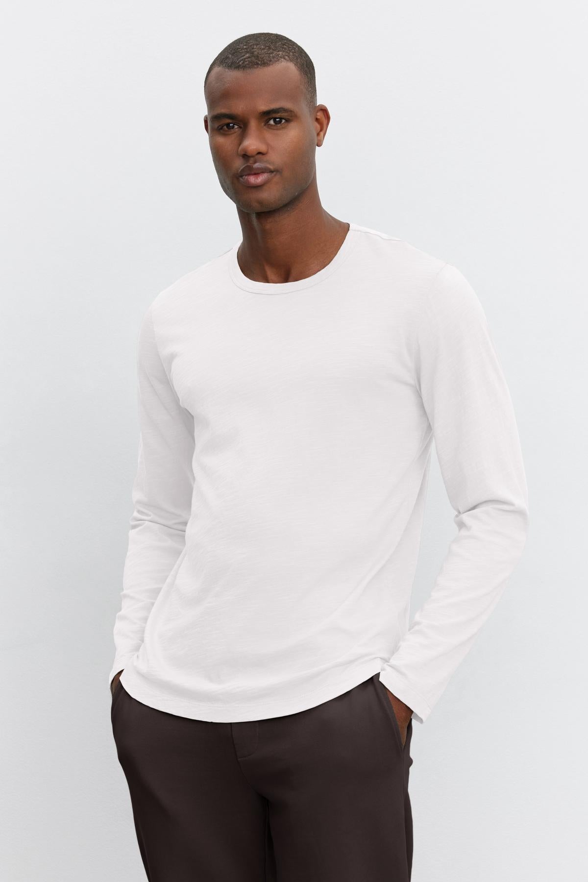   A man in a Velvet by Graham & Spencer KAI CREW NECK TEE and dark trousers stands against a light gray background, looking directly at the camera. 