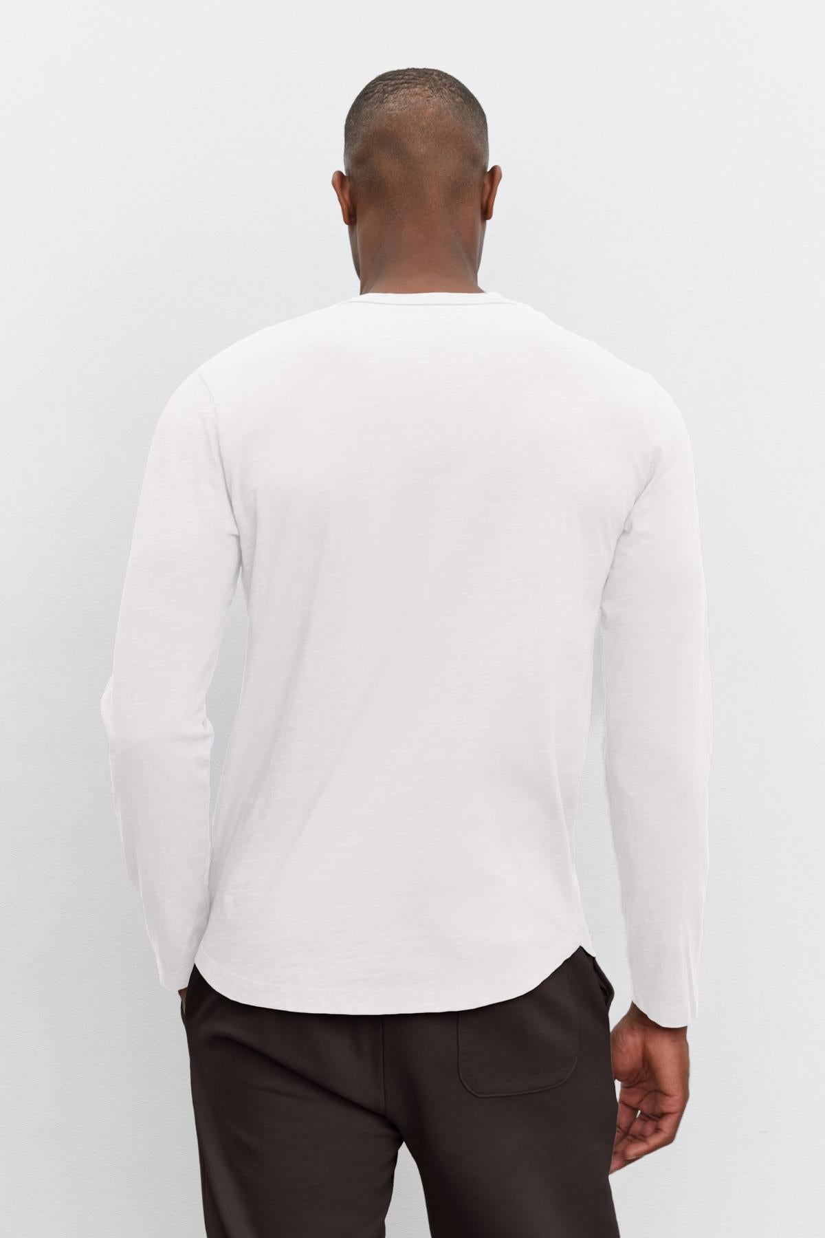   Rear view of a man wearing a Velvet by Graham & Spencer KAI CREW NECK TEE and brown trousers, standing against a grey background. 