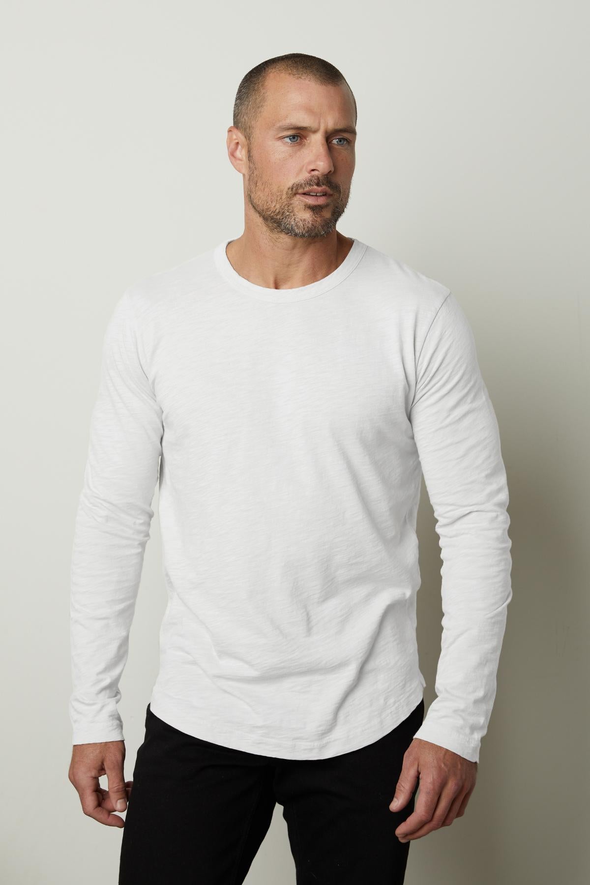 A man wearing a flawless fit white long sleeve KAI CREW NECK TEE by Velvet by Graham & Spencer, the perfect layering piece.-35855337521345