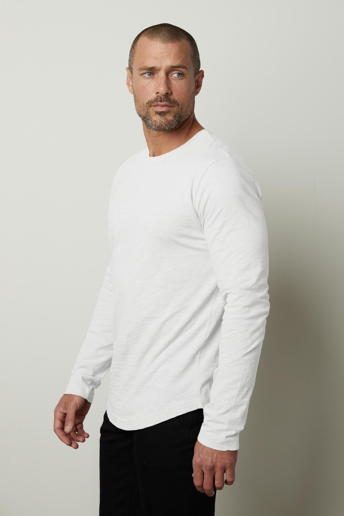   A man wearing a flawless fit white long sleeve KAI CREW NECK TEE, perfect as a layering piece in slub knit fabric by Velvet by Graham & Spencer. 