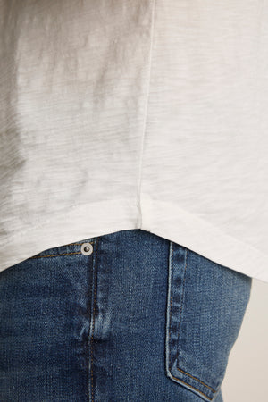 Close-up of a person wearing the KAI TEE by Velvet by Graham & Spencer, featuring a white classic crew neckline and blue jeans, highlighting the textures and stitches of its Peruvian cotton fabric.