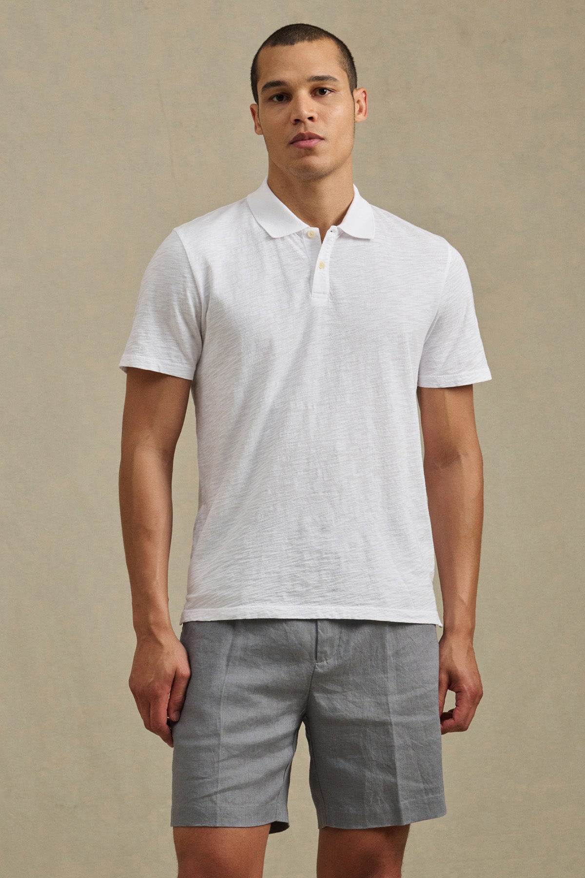 A man stands facing forward, wearing the white MORRIS POLO by Velvet by Graham & Spencer and light gray shorts against a neutral background.-41384130707649