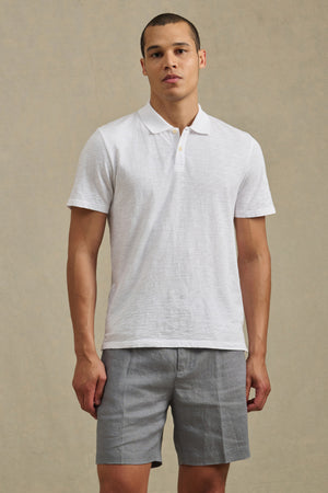A man stands facing forward, wearing the white MORRIS POLO by Velvet by Graham & Spencer and light gray shorts against a neutral background.