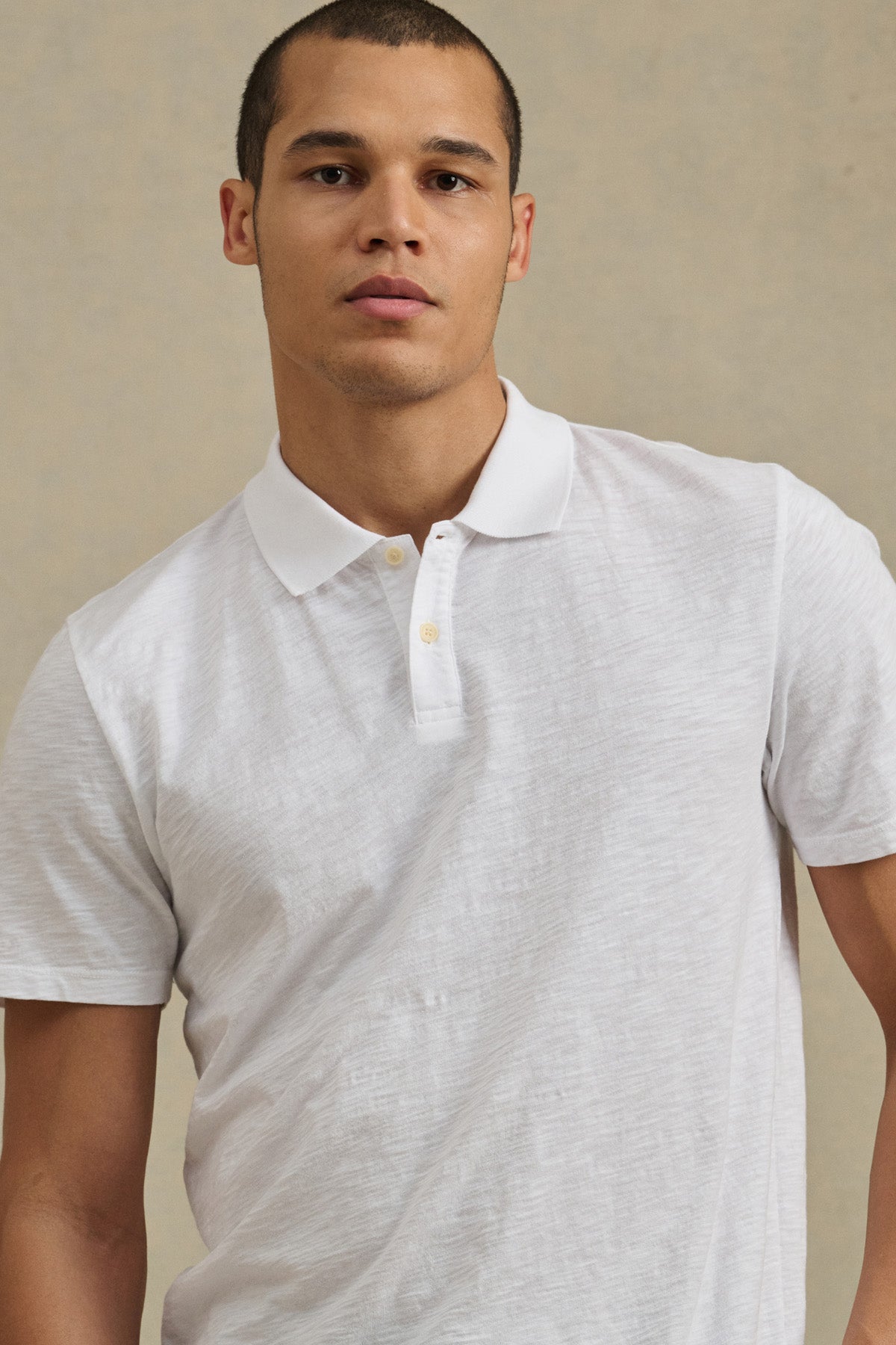 A man wearing the MORRIS POLO by Velvet by Graham & Spencer, a white cotton slub polo with a two-button placket, stands before a neutral background, facing the camera.