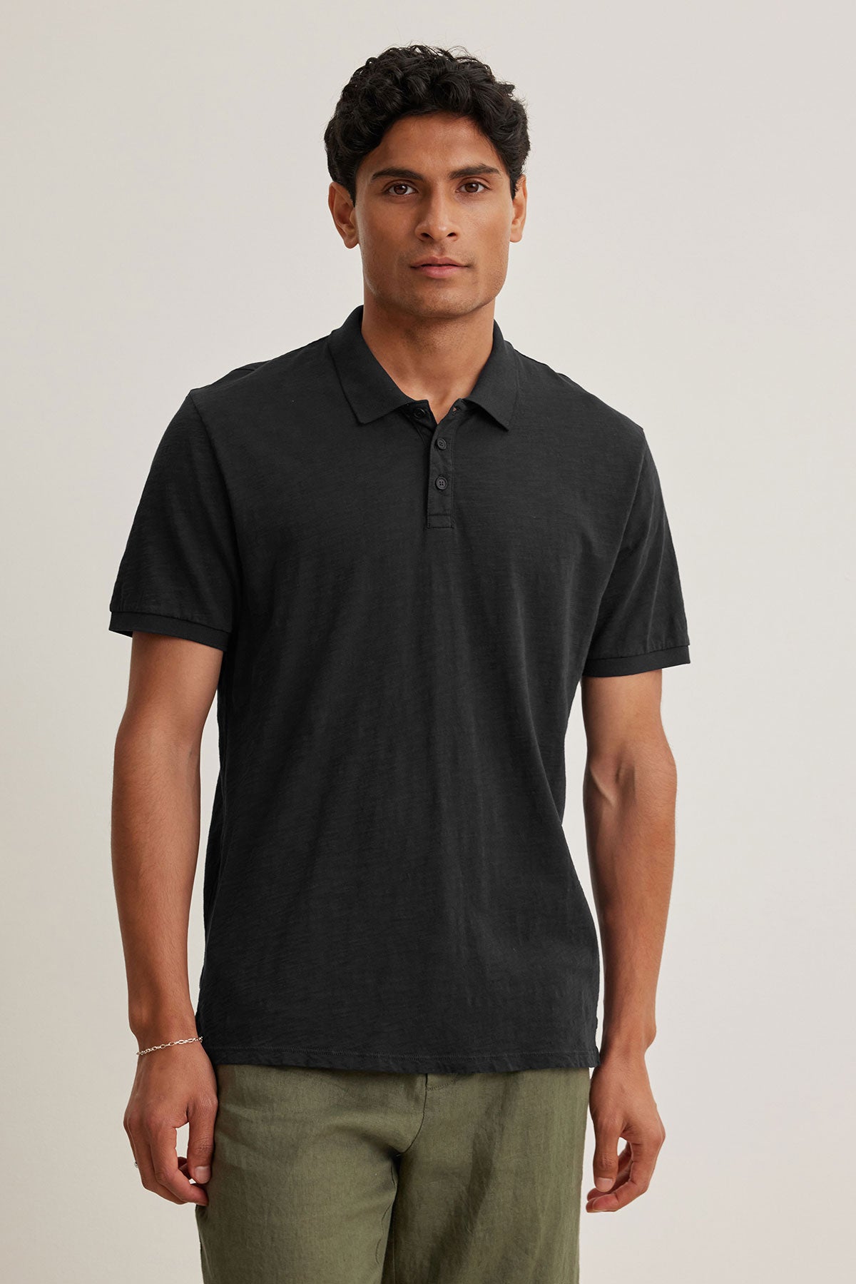 A man in a NIKO POLO by Velvet by Graham & Spencer, made from luxurious Peruvian cotton, and green pants stands against a plain background.-38800733733057