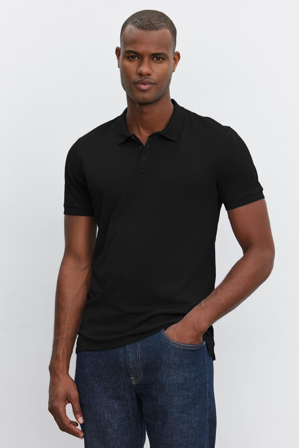   A man wearing a black heathered texture NIKO POLO shirt and blue jeans standing against a white background, looking at the camera with a neutral expression. (Brand Name: Velvet by Graham & Spencer) 