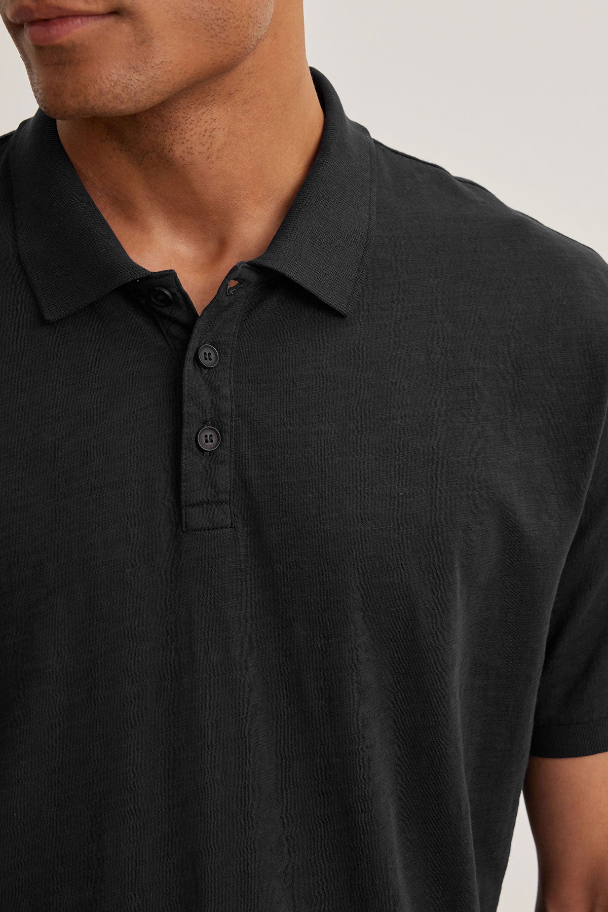 An individual in a NIKO POLO by Velvet by Graham & Spencer, crafted from soft Peruvian cotton with a buttoned collar, faces left while wearing a black polo shirt.-38800733831361