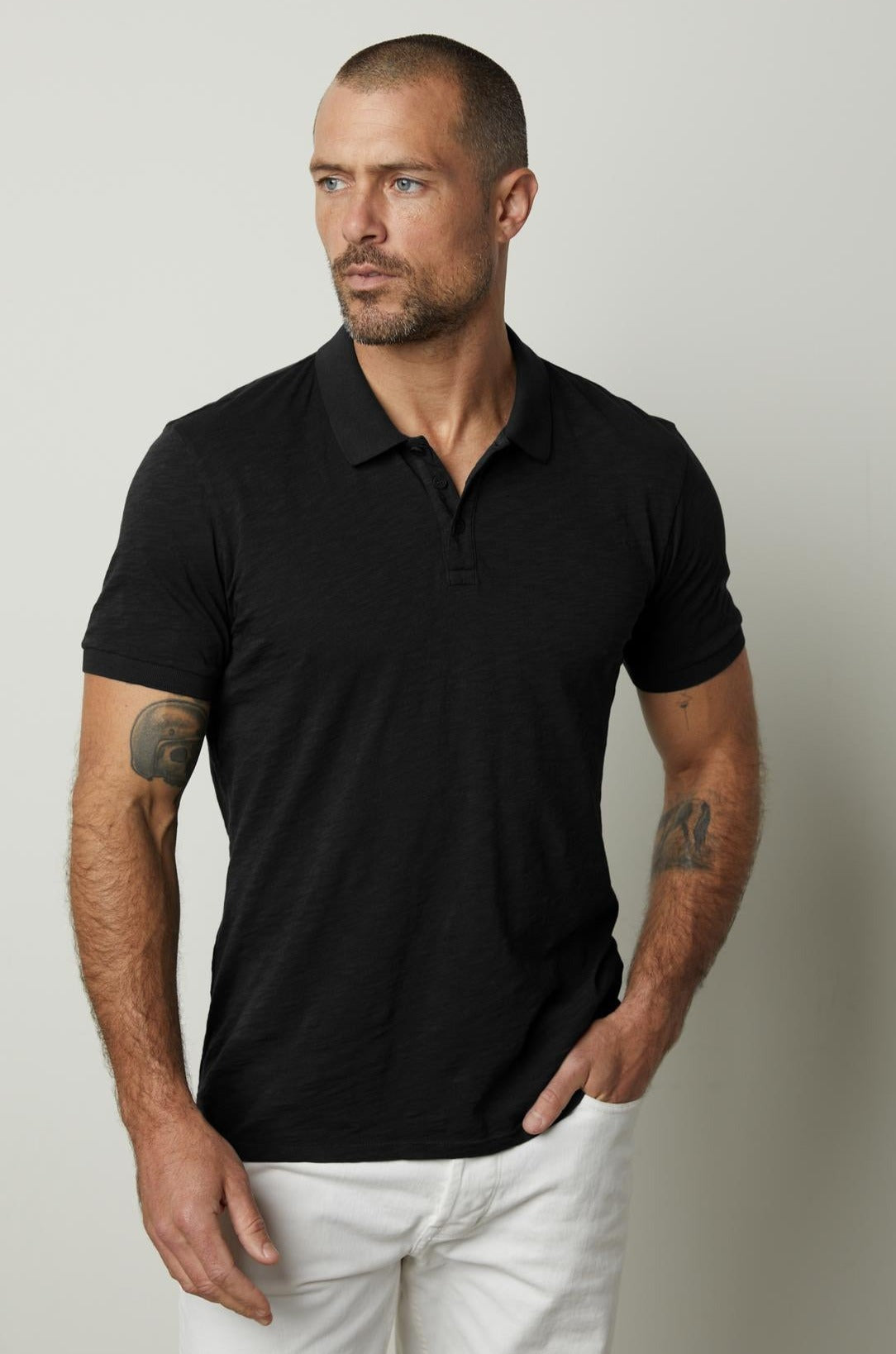   A man wearing a black NIKO POLO shirt by Velvet by Graham & Spencer and white pants. 