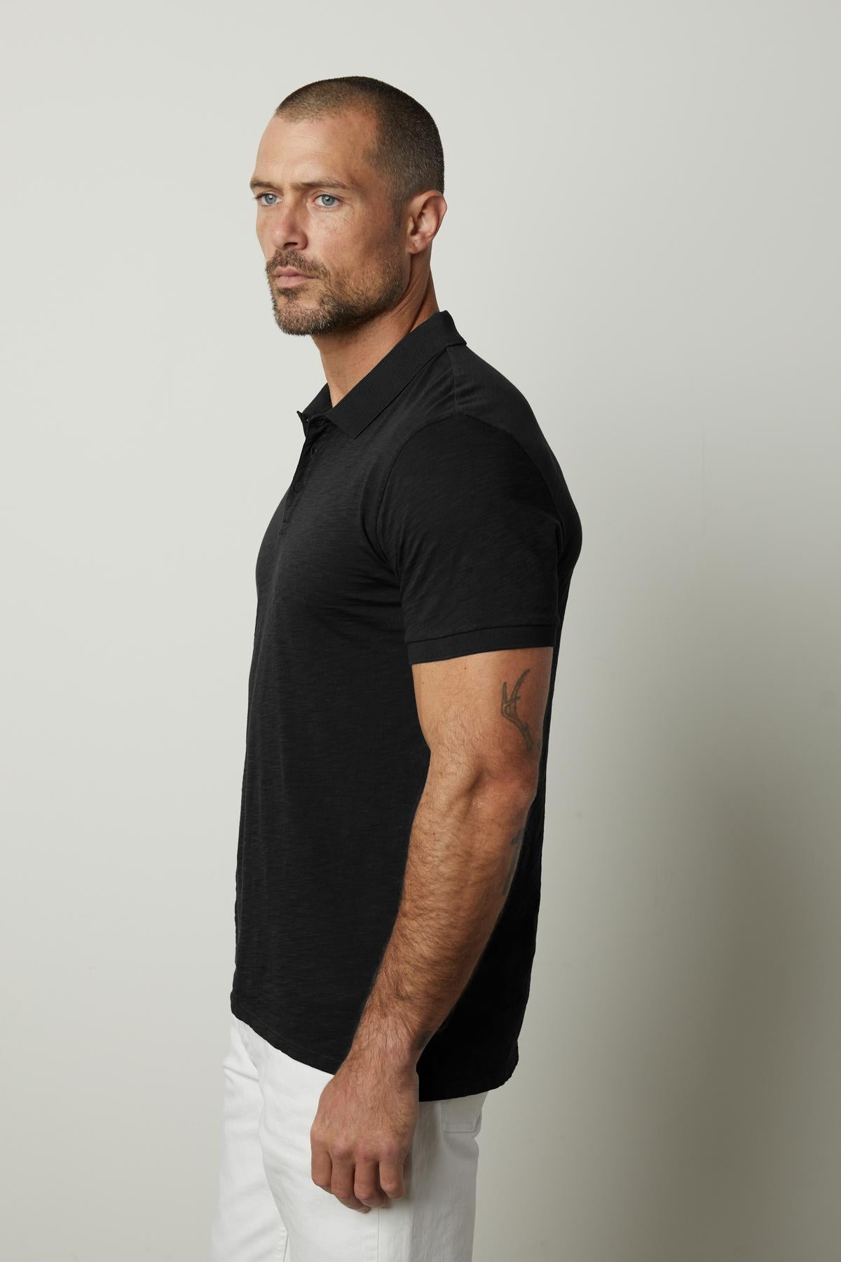   A man wearing a black NIKO POLO shirt and white pants by Velvet by Graham & Spencer. 