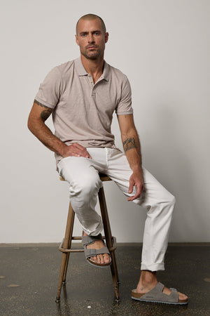 A man sitting on a stool wearing a NIKO POLO shirt by Velvet by Graham & Spencer and white pants.