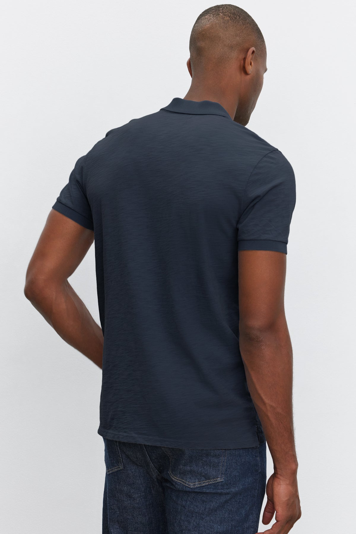 Rear view of a man wearing a Velvet by Graham & Spencer NIKO polo shirt with heathered texture and denim jeans, standing against a white background.-36890752811201