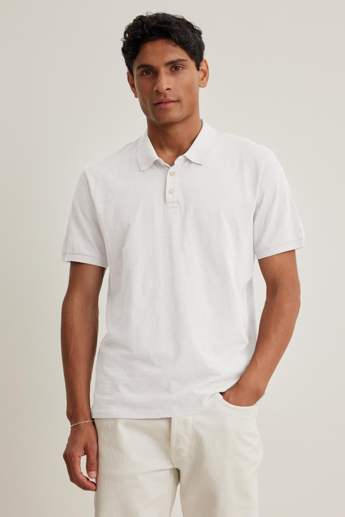   A person wears the NIKO POLO and matching white pants from Velvet by Graham & Spencer, made with soft Peruvian cotton, against a plain background. 