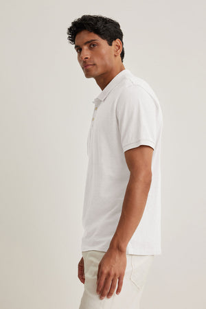 A man wearing the NIKO POLO by Velvet by Graham & Spencer, made from lightweight cotton, and beige pants stands sideways against a plain background, highlighting the versatility of this ensemble.