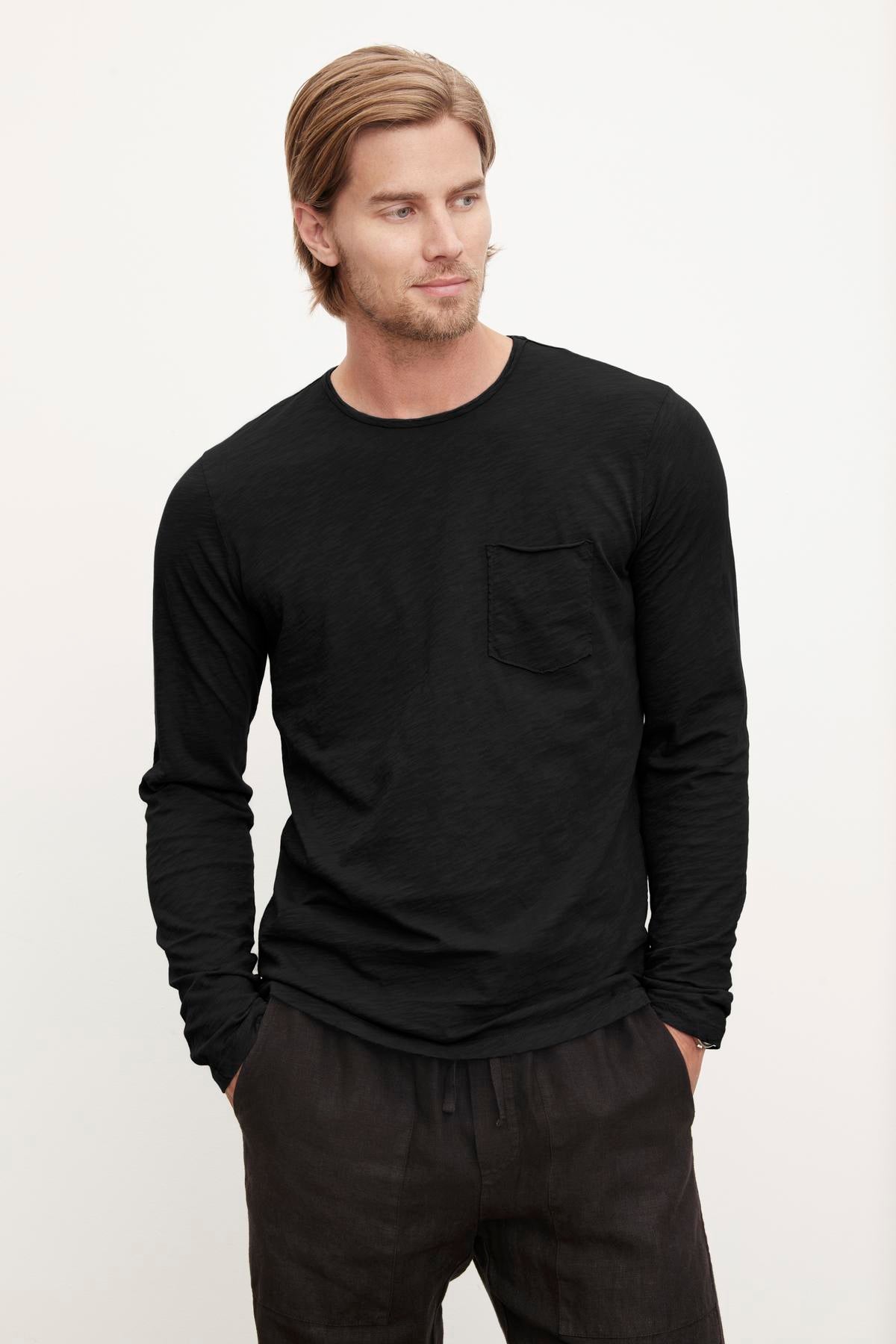 Man wearing a black long-sleeve SIMEON RAW EDGE COTTON SLUB TEE by Velvet by Graham & Spencer posing with his hands in his pockets.-36418291171521