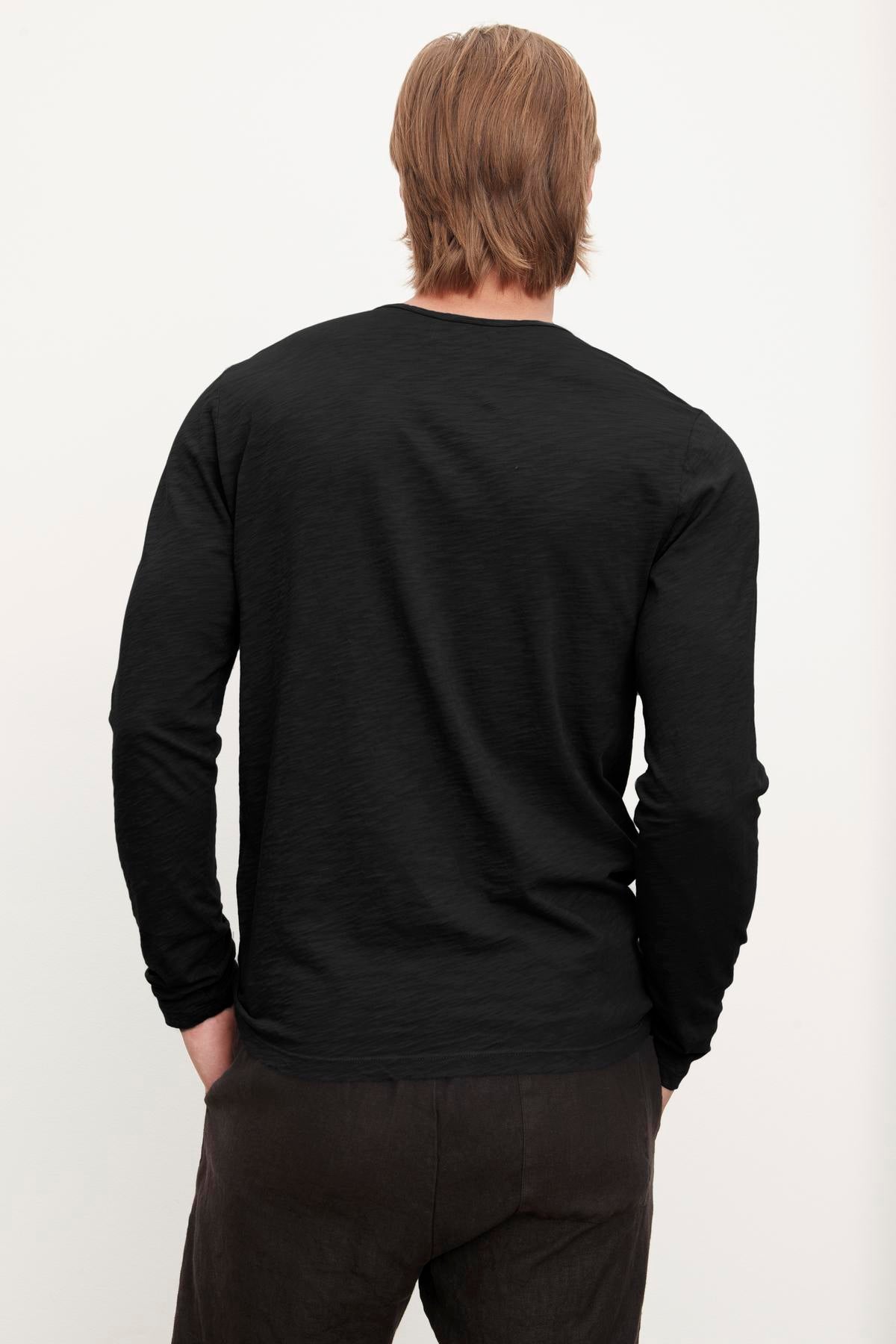 A person with long hair, wearing a black long-sleeved SIMEON RAW EDGE COTTON SLUB TEE by Velvet by Graham & Spencer, photographed from the back, embodying California heritage.-36418291138753