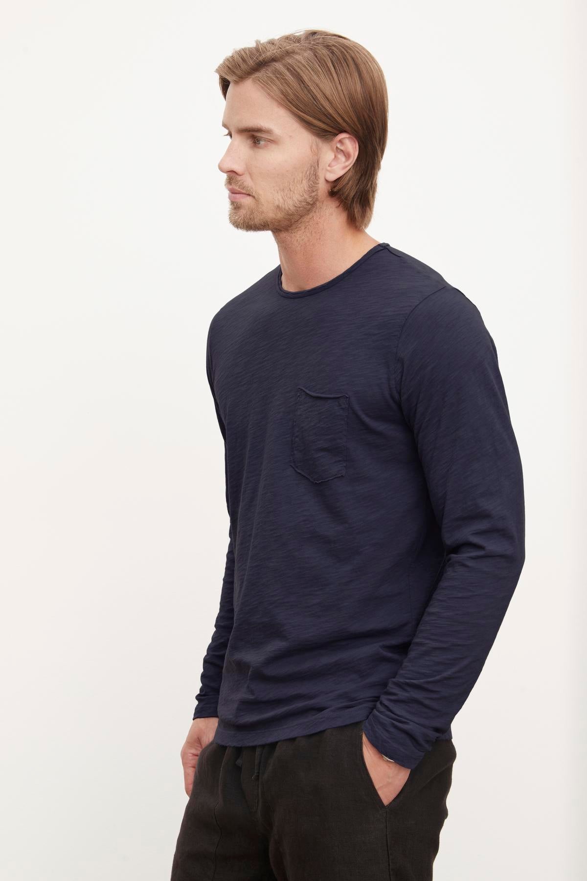 Man standing side profile wearing a Velvet by Graham & Spencer SIMEON RAW EDGE COTTON SLUB TEE with a pocket and black pants.-36418292121793