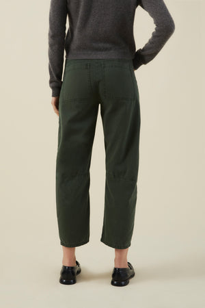 Back view of dark green BRYLIE PANT cotton twill barrel leg trousers with utilitarian patch pockets, worn with a grey sweater and black loafers.