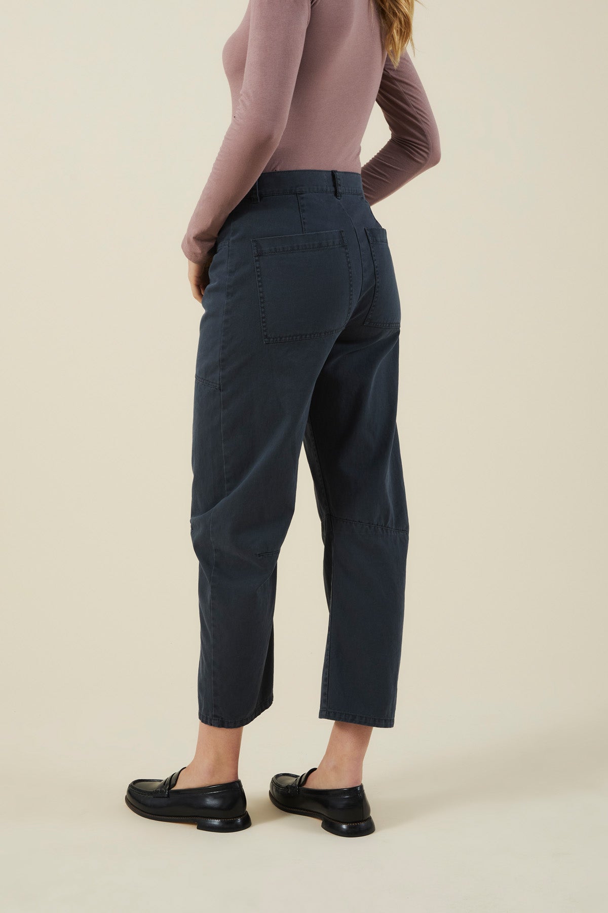 A person from behind wearing dark-colored BRYLIE PANT barrel leg pants with utilitarian patch pockets and black loafers.-46488162730177
