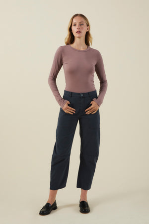 A model wears a long-sleeved dusty mauve shirt, dark cotton twill BRYLIE PANT with utilitarian patch pockets, and black loafers.