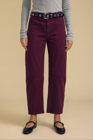A person wearing a gray long-sleeve top, the BRYLIE PANT by Velvet by Graham & Spencer—structured burgundy cotton twill barrel leg trousers with utilitarian patch pockets—a black belt with grommets, and black ballet flats, standing against a beige background.
