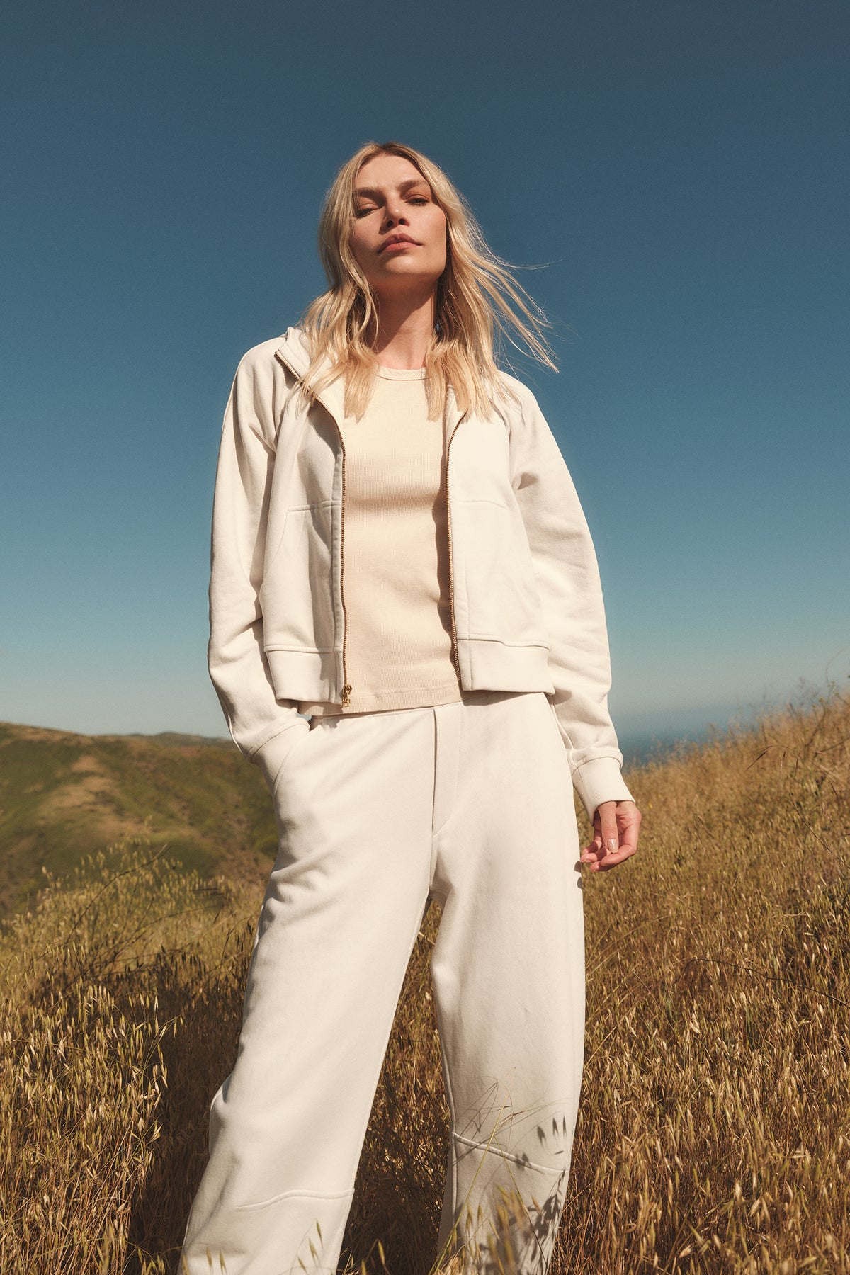 A woman standing in a field wearing the TORY SOFT FLEECE HOODIE by Velvet by Graham & Spencer.-35696175251649