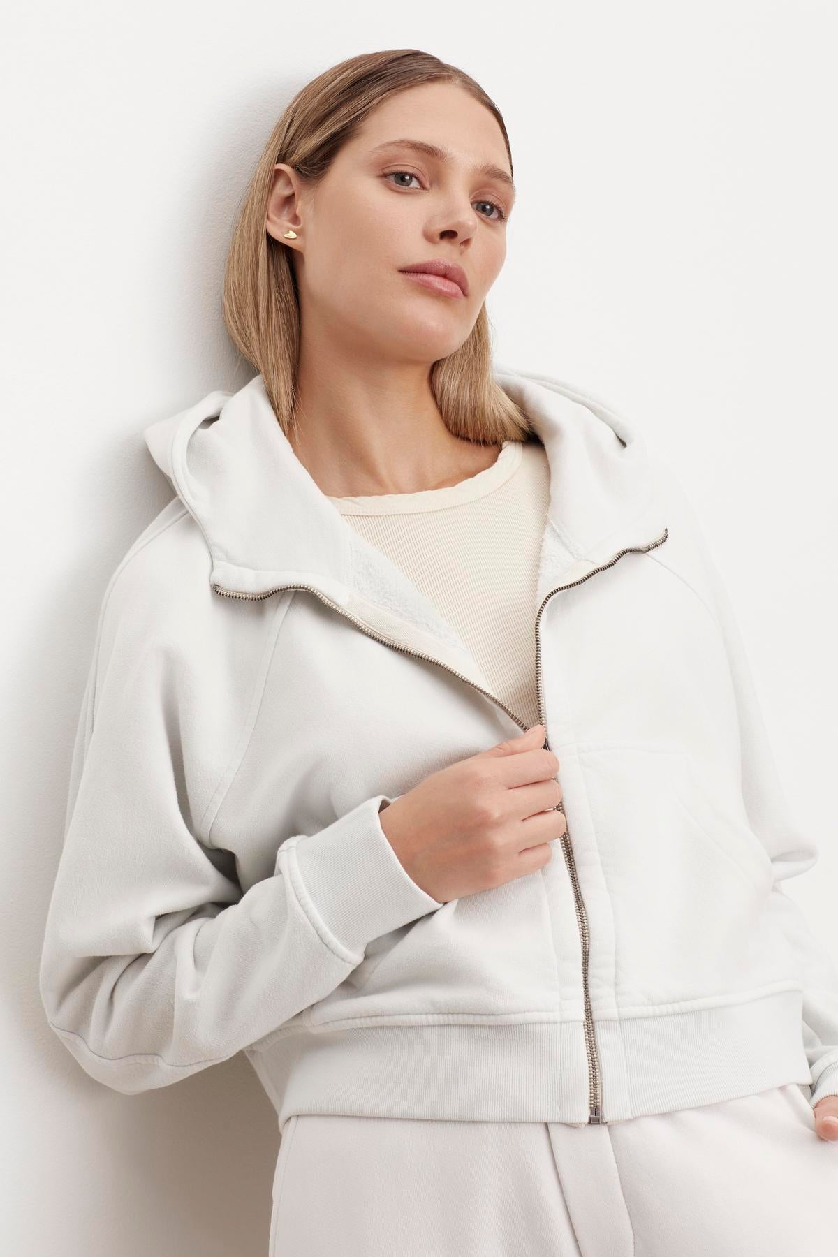 The model is wearing a white Velvet by Graham & Spencer TORY SOFT FLEECE HOODIE.-35696175284417